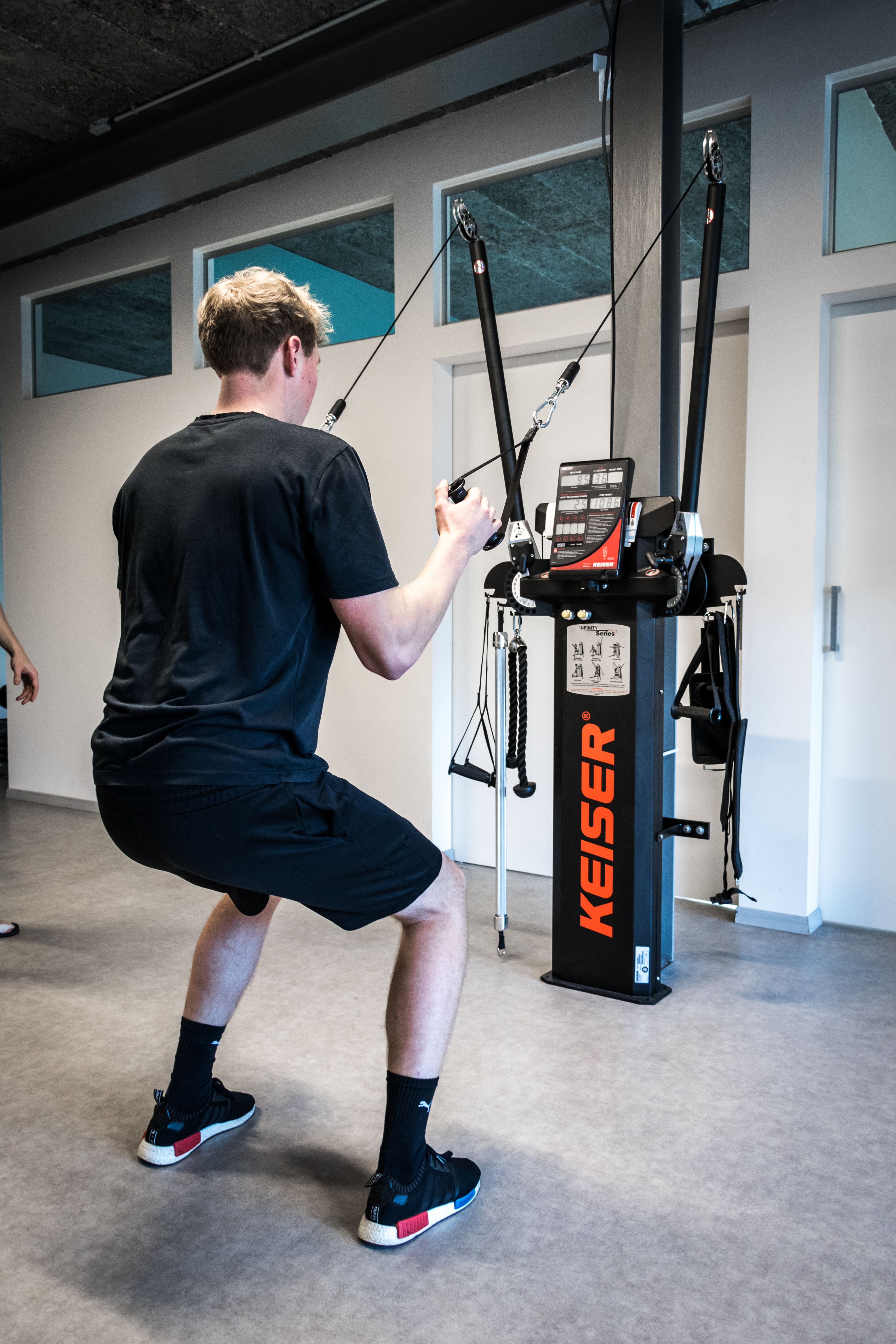 Een jonge man die met een kabeltrekmachine van Keiser in een fitnessruimte traint.