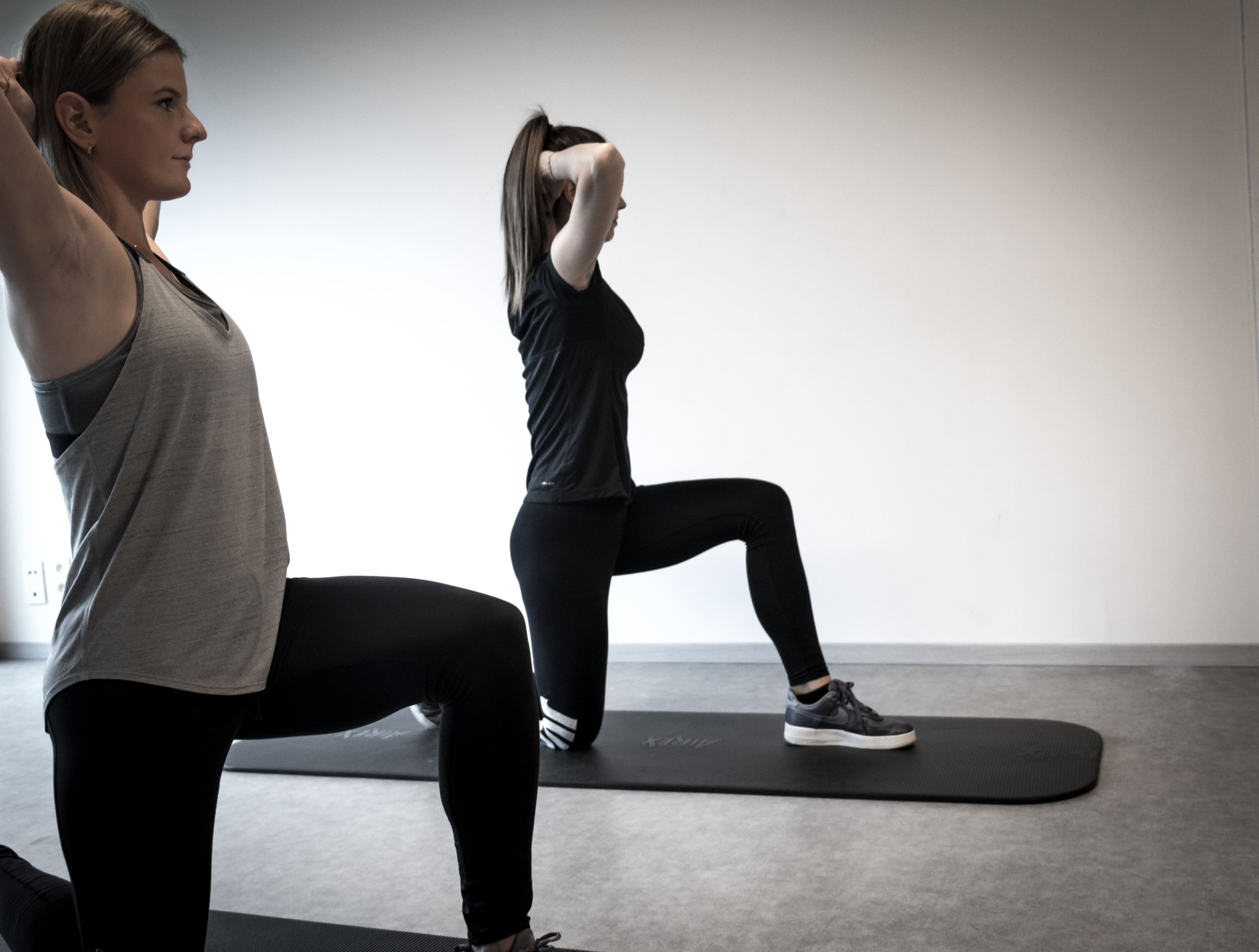 Twee vrouwen die knie-oefeningen doen op fitnessmatten in een rustige ruimte.