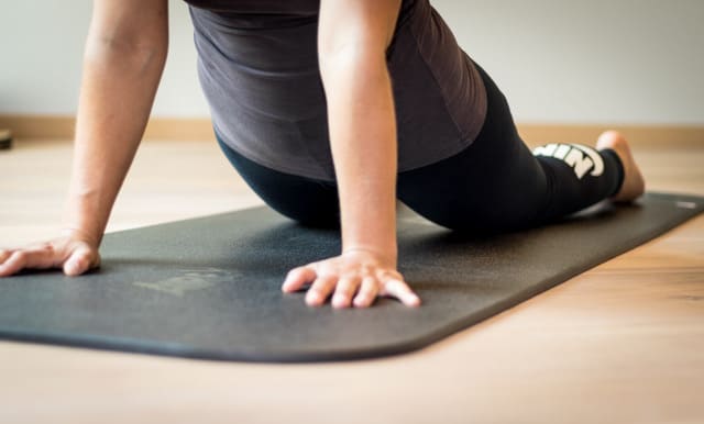 Persoon doet yoga-oefening op zwarte mat in huiselijke omgeving.