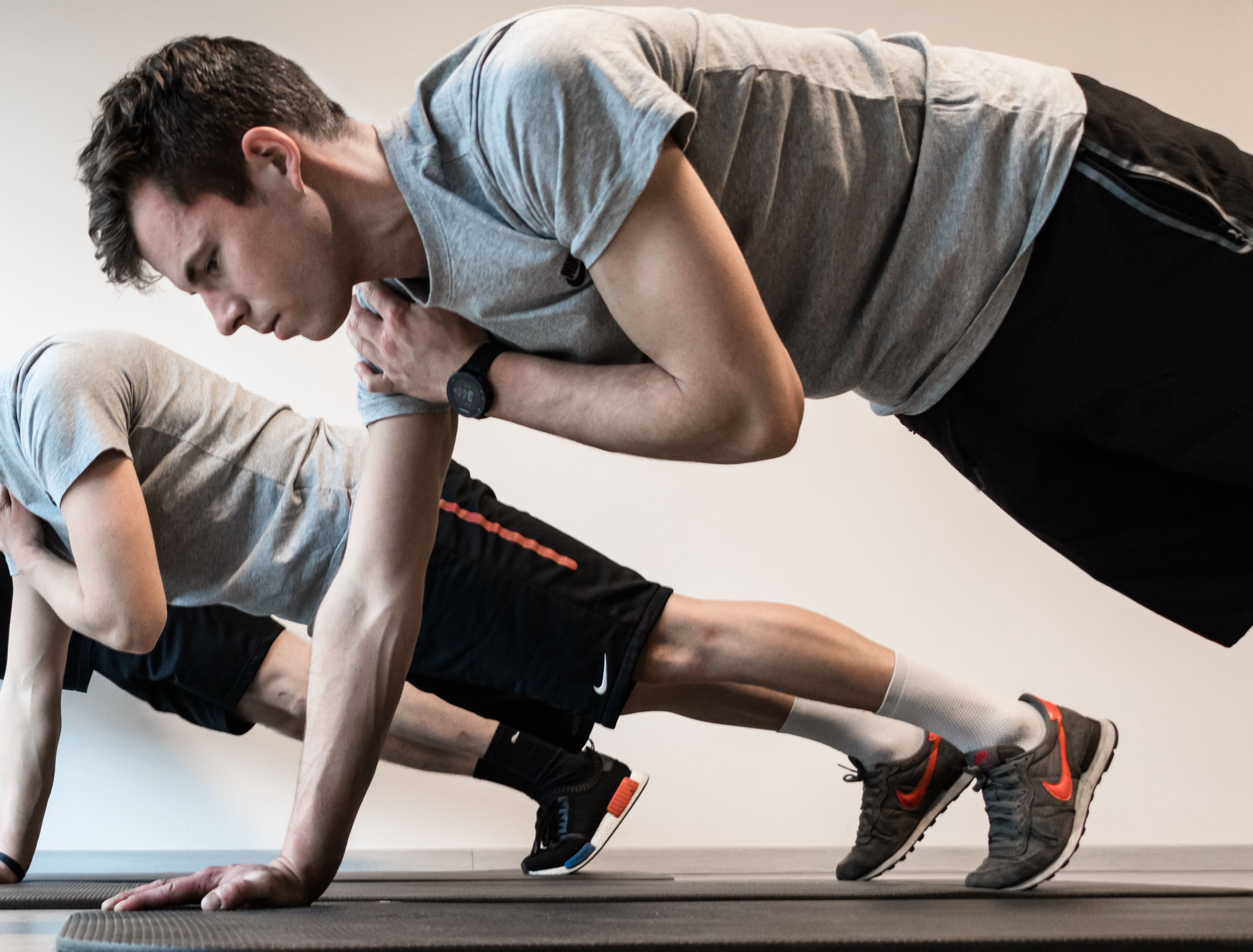 Twee jonge mannen doen oefeningen met plankvariaties op yogamatten in een lichte kamer.