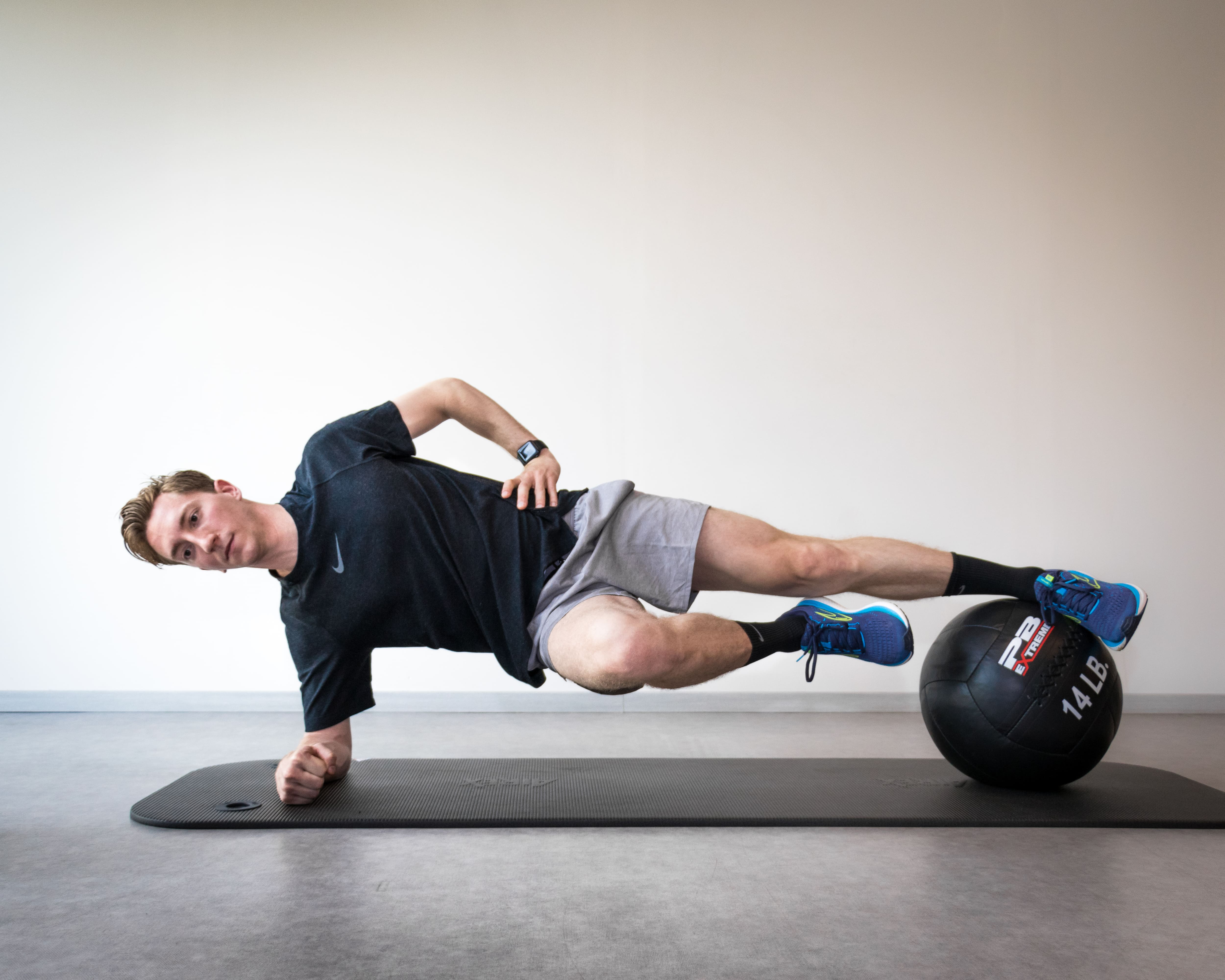 Man voert een zijplank uit op een fitnessmat met voeten op een medicijnbal van 14 lbs.