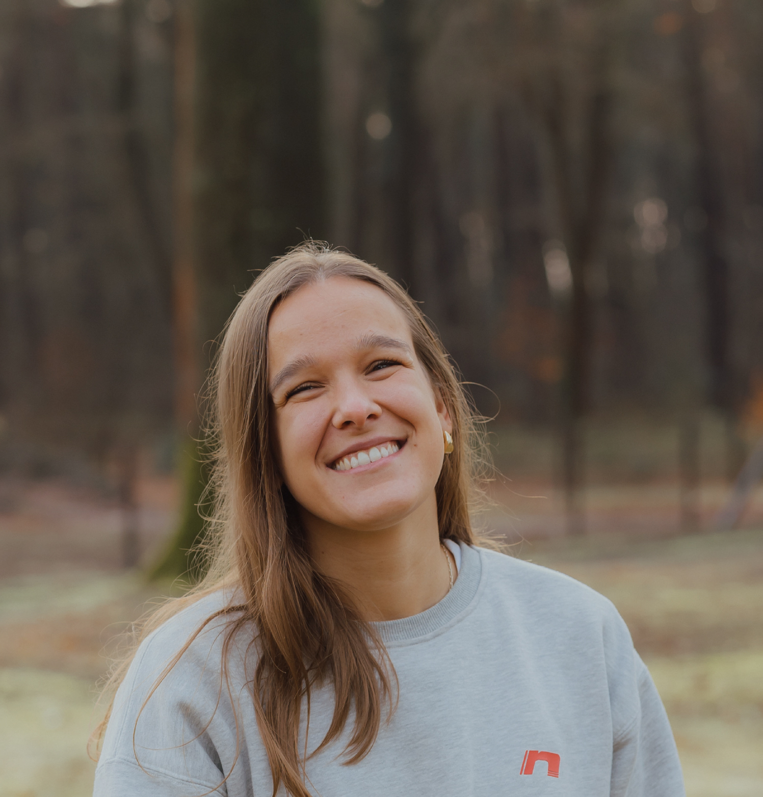 Jonge vrouw met lang bruin haar lacht naar de camera tegen een lichte achtergrond.