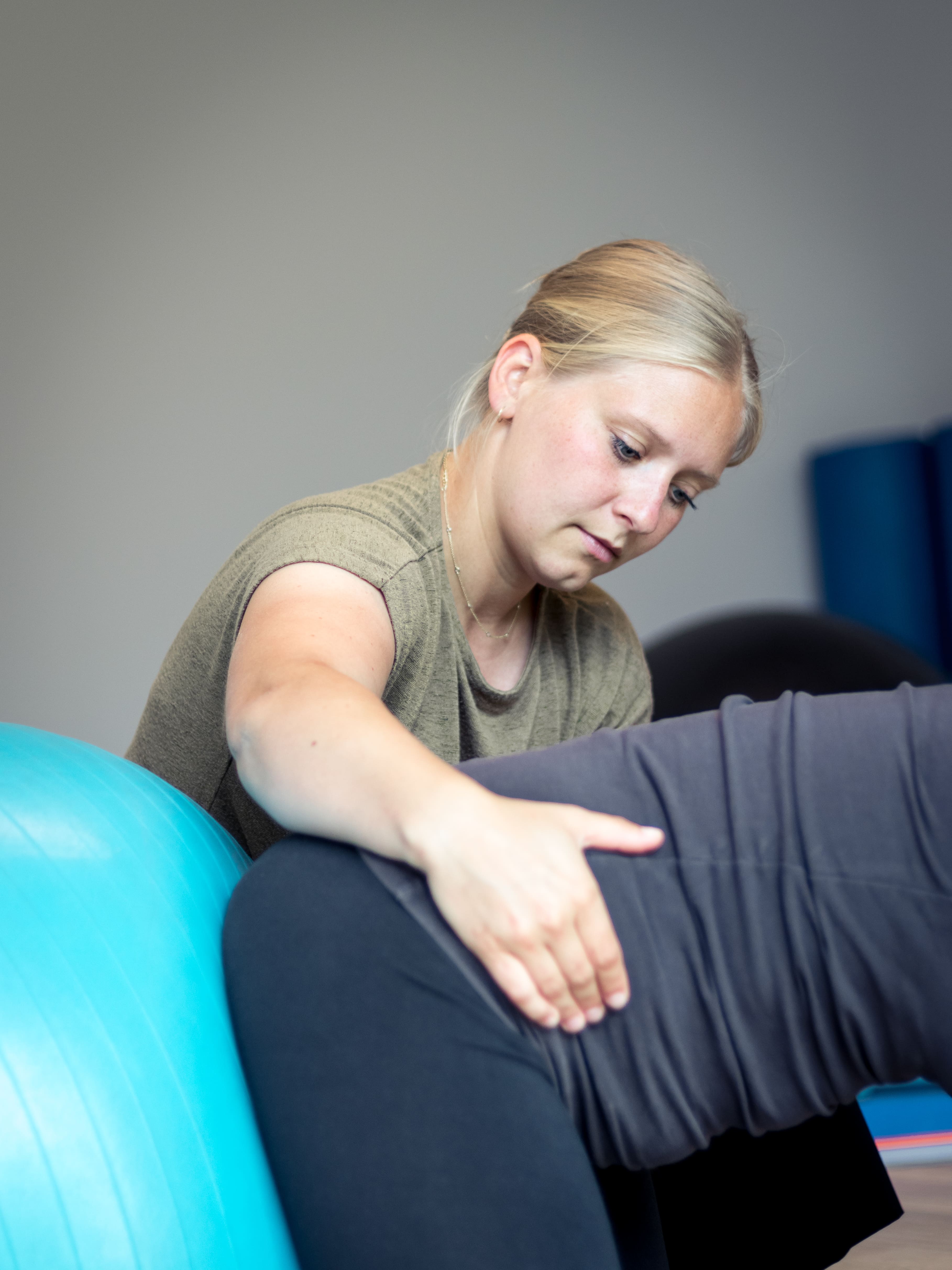 Fysiotherapeut helpt patiënt met oefeningen op een blauwe oefenbal.