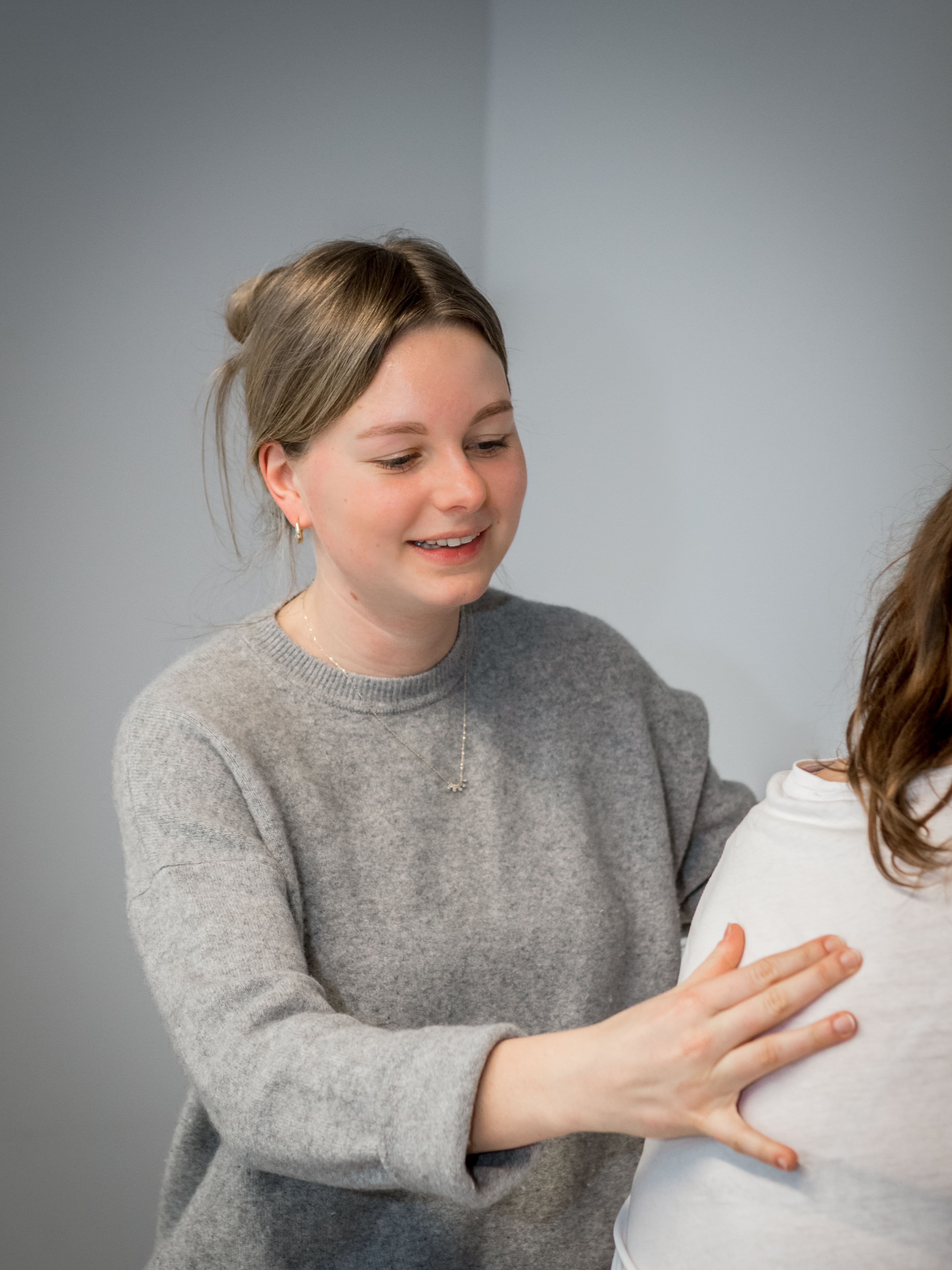 Jonge vrouw in een grijze trui die vriendelijk haar hand op de rug van een ander legt.