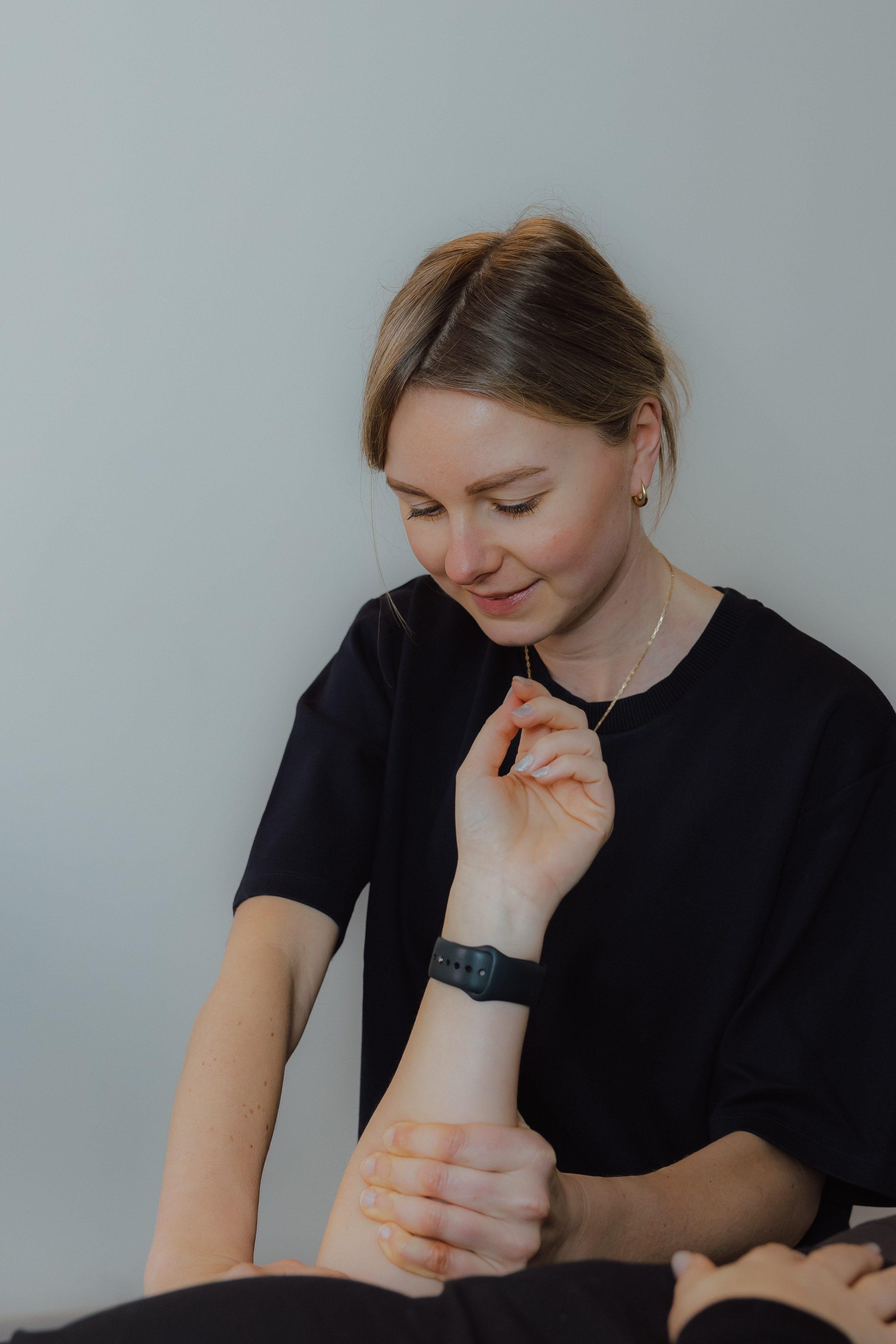 Vrouw die de pols van een andere persoon vasthoudt en onderzoekt, met een zachte glimlach.