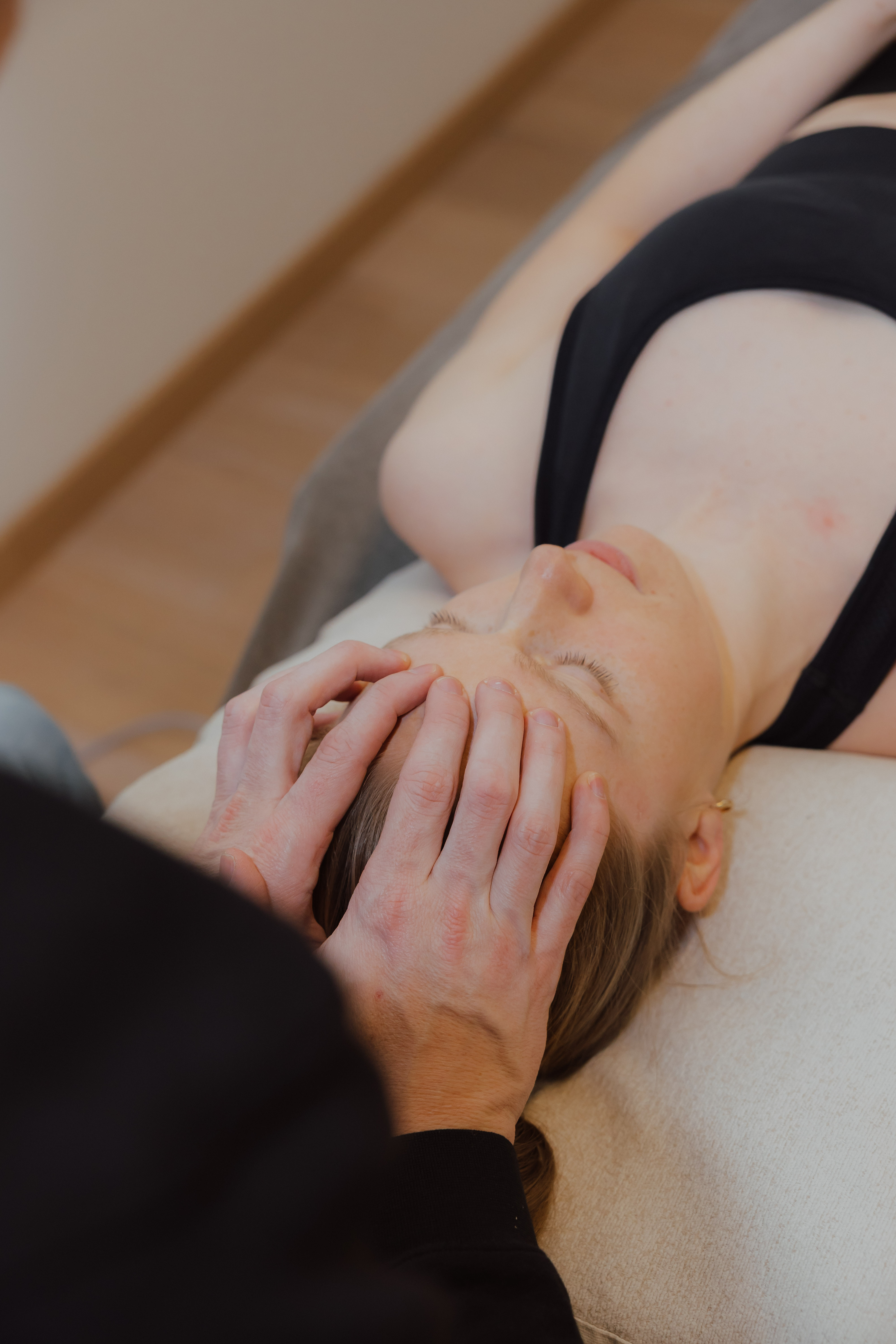 Een vrouw ligt op een massagetafel terwijl iemand haar voorhoofd zachtjes masseert.