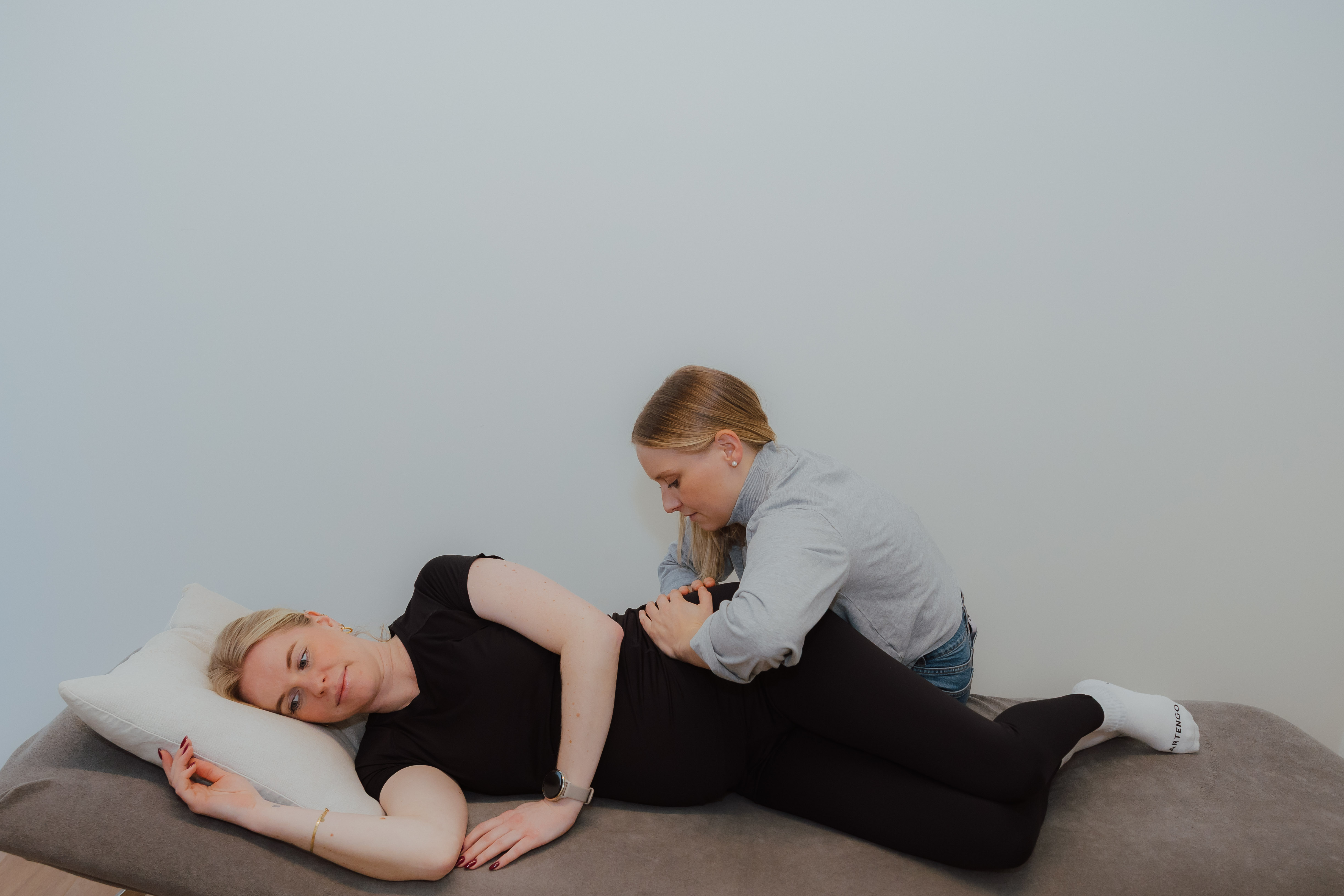 Een vrouw ligt op haar zij op een massagebank terwijl een therapeut haar heup masseert.