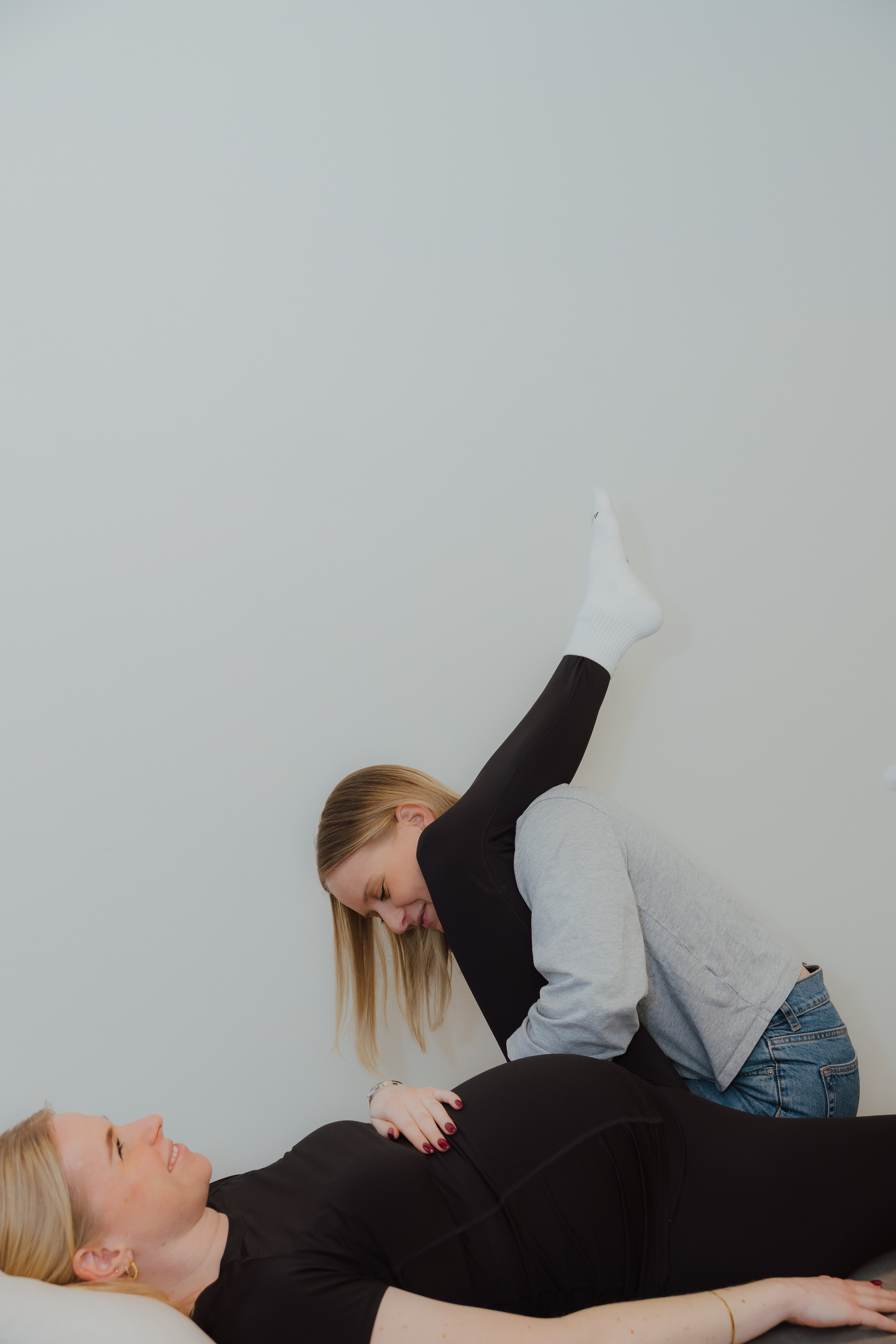 Een vrouw die een andere vrouw helpt met het stretchen van haar been terwijl ze op een mat ligt.