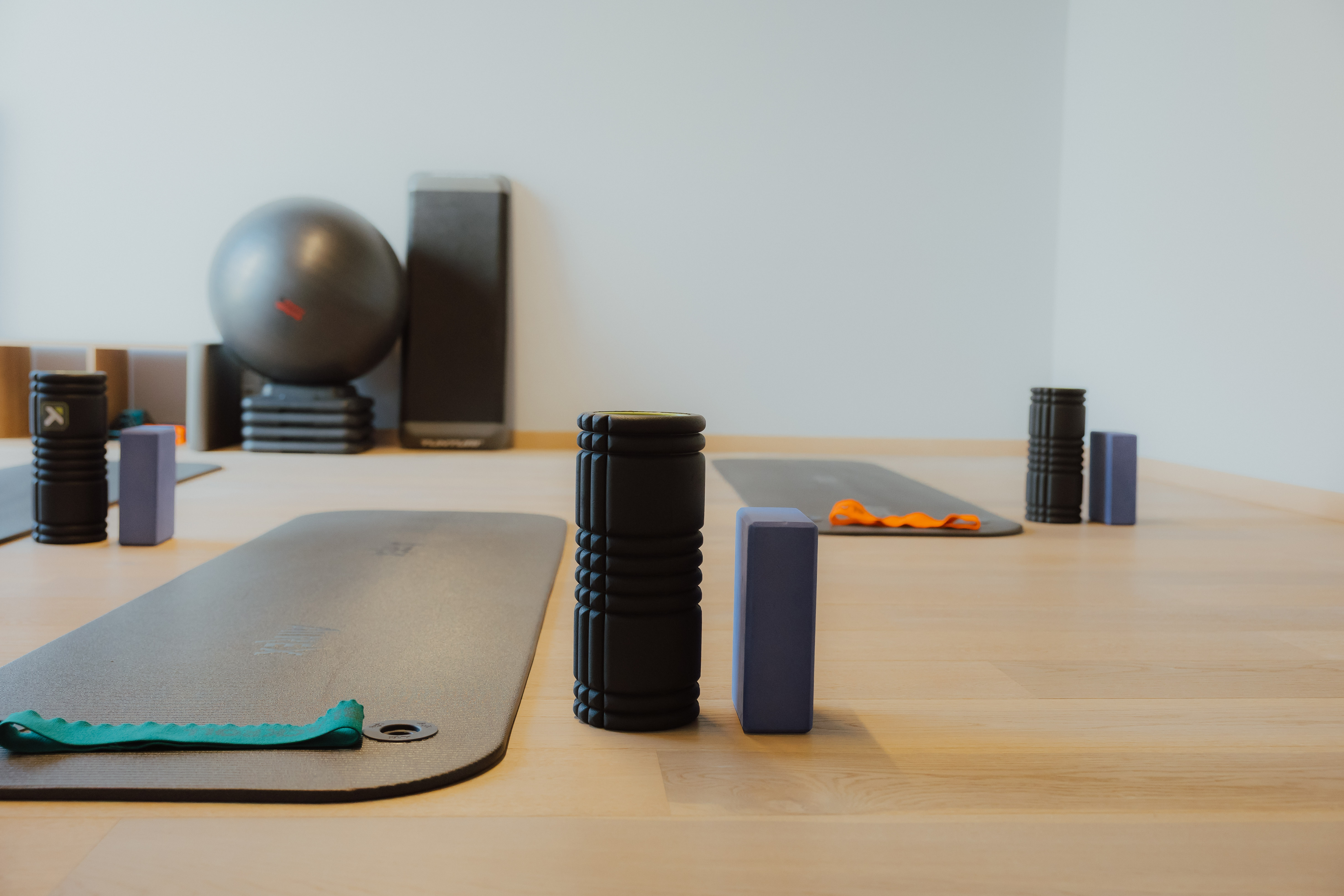 Yoga matten, schuimrollers en yoga blokken klaar voor gebruik in een lichte fitnessruimte met een grote fitnessbal en stapels oefenmatten aan de achterzijde.