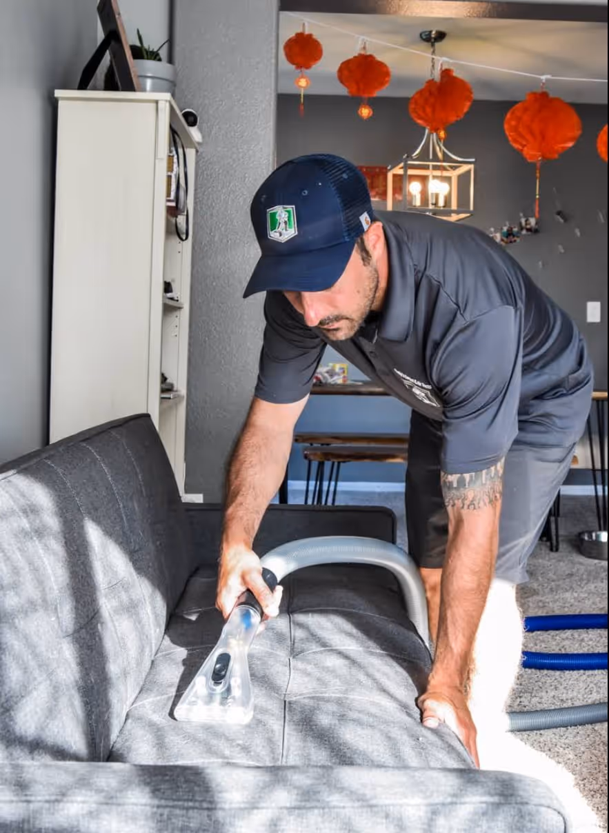 Matty, the owner of Mattys Carpet & Air Duct Cleaning out of Thornton CO preforming Upholstery cleaning on a couch in a living room using a water extraction tool
