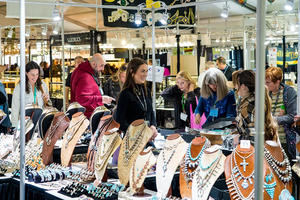Wholesale buyers and exhibitors networking at GLW Tucson Gem Show with jewelry display cases and vendor booths