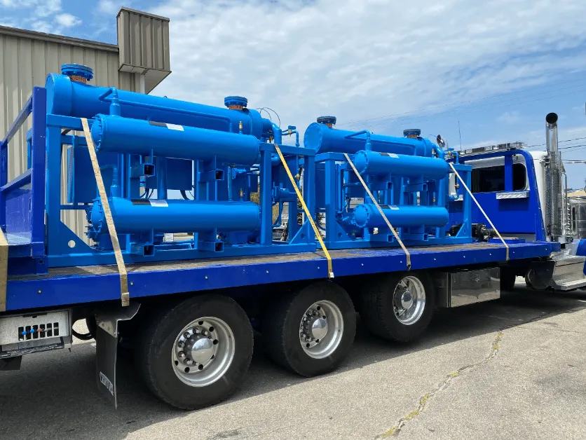 Blue semi-truck carrying large industrial refrigeration equipment secured with straps on a flatbed trailer.