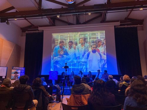 A dimly lit room filled with attendees gathered in solidarity at a Manhattan event honoring Dalit scholar Rohith Vemula on his birth anniversary, January 30, 2026.