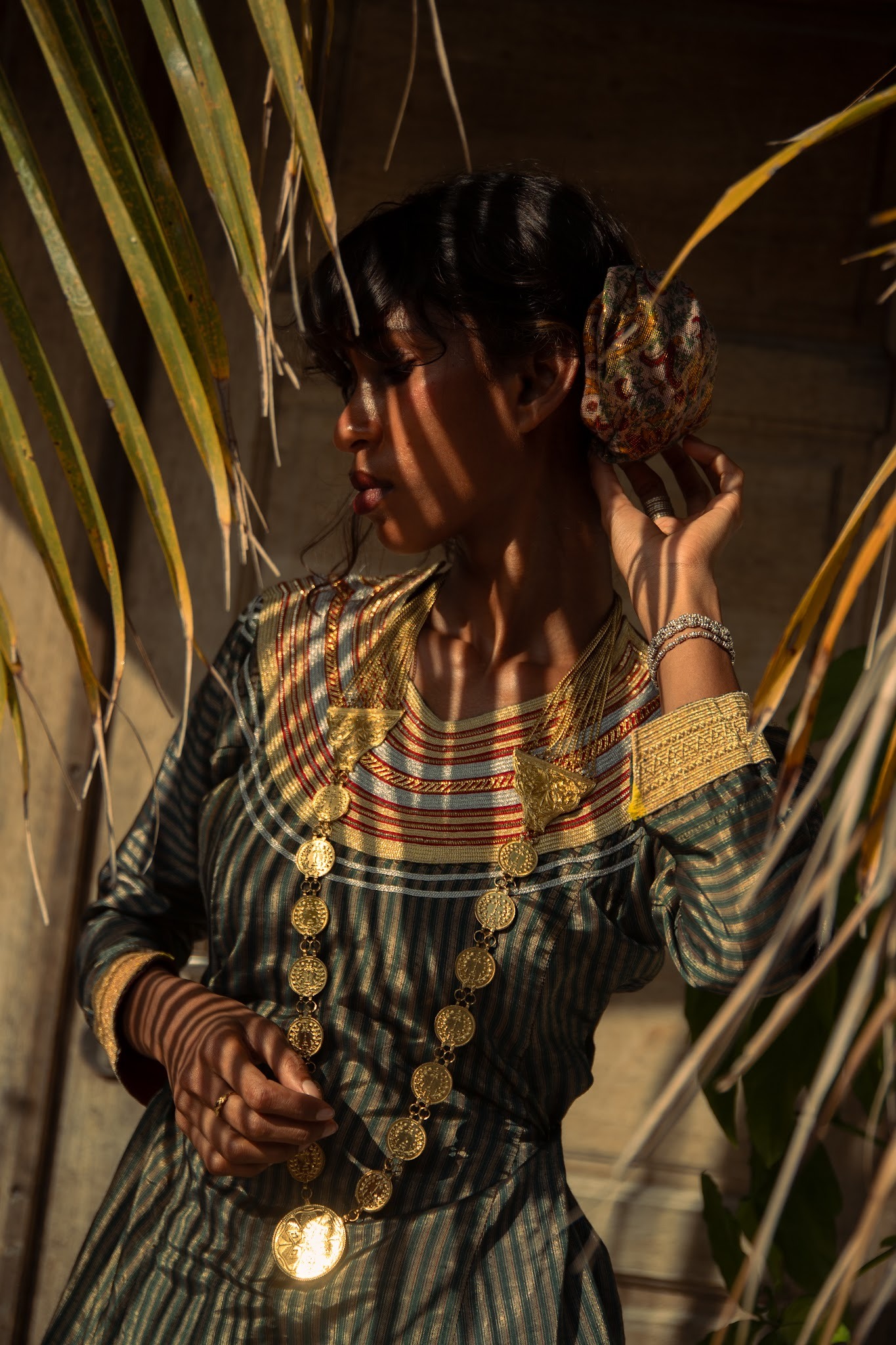 Picture of Zami touching her hair and posing sideways from the camera under shadows of palm trees.