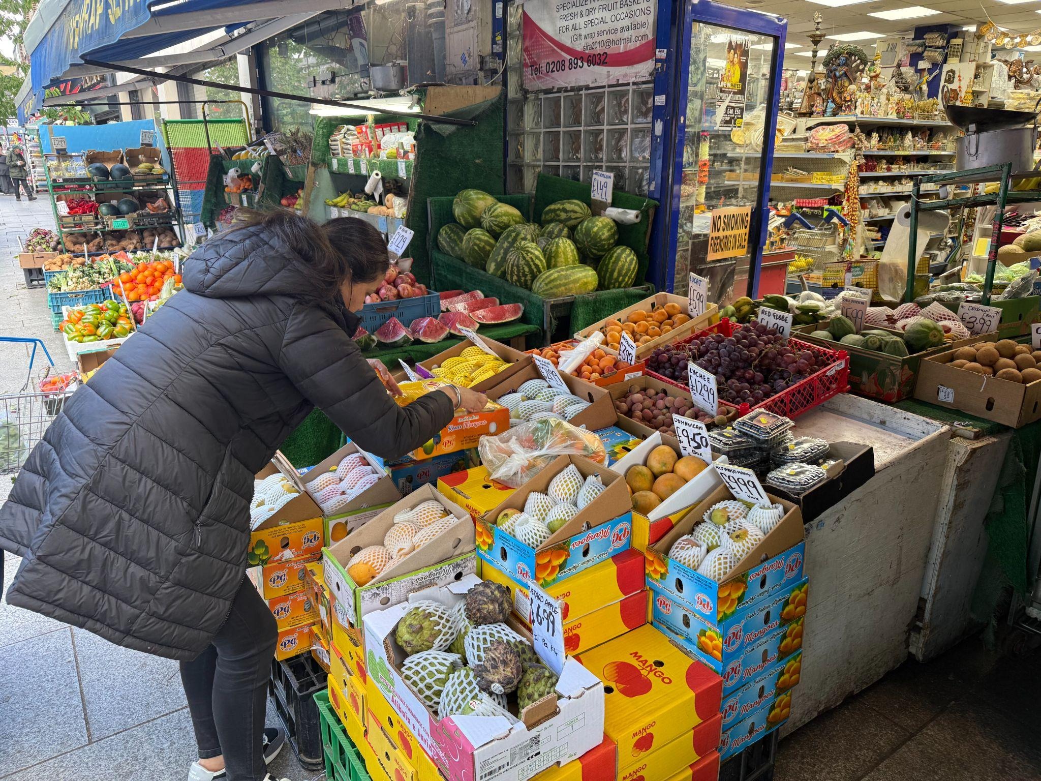 A customer shops for mangoes in front of a shop.