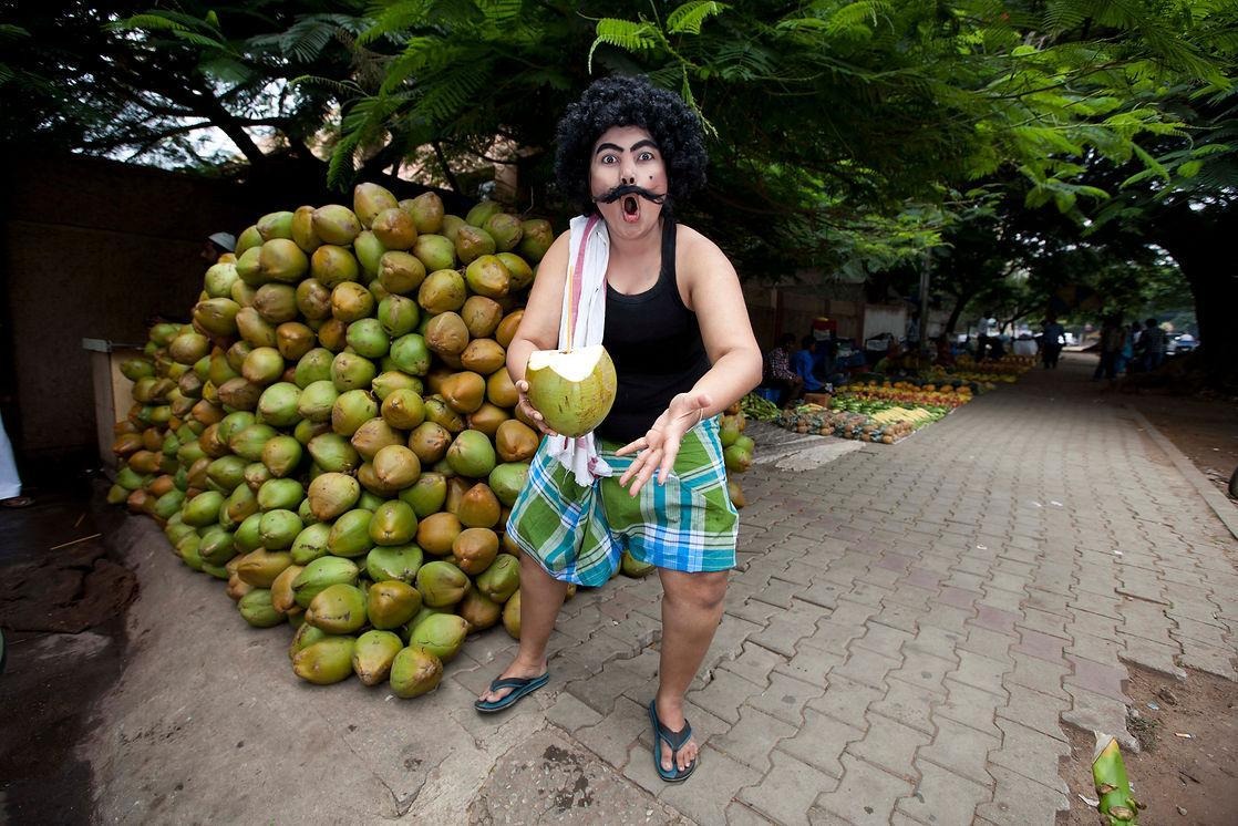 A drag king dressed as a coconut seller pictured in front of a tender coconut stall on a footpath in Bangalore