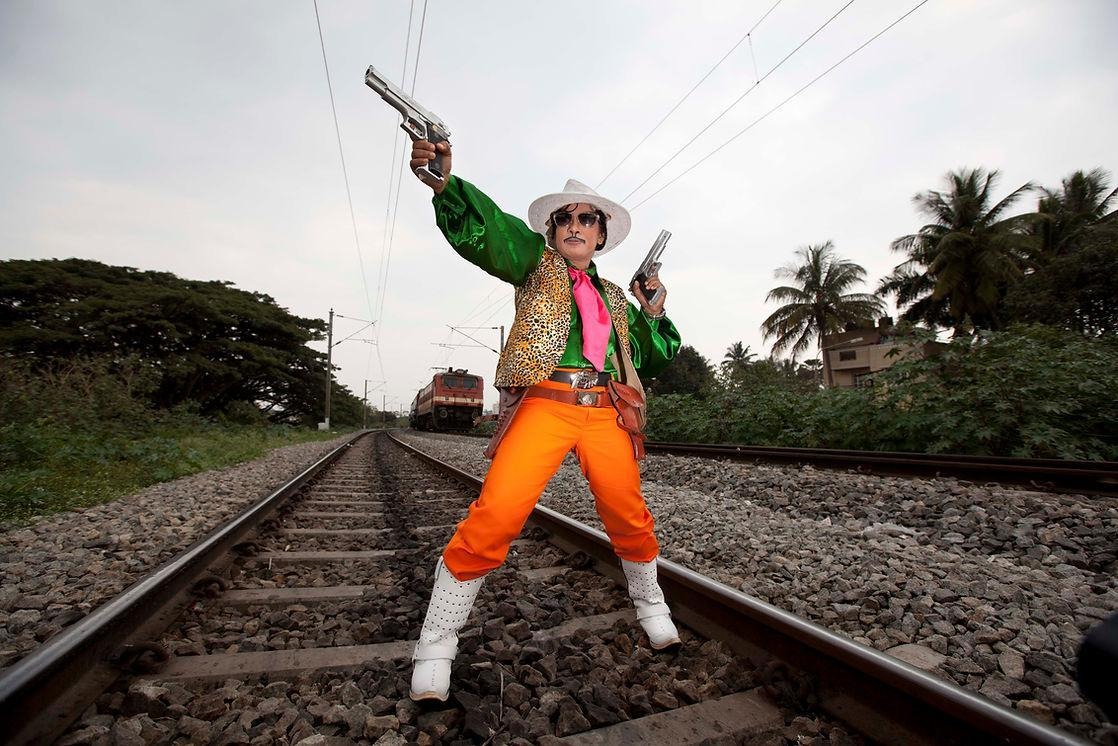 A drag king dressed as Quick Gun Murugan pictured on a railway track in Bangalore with the train appearing behind them