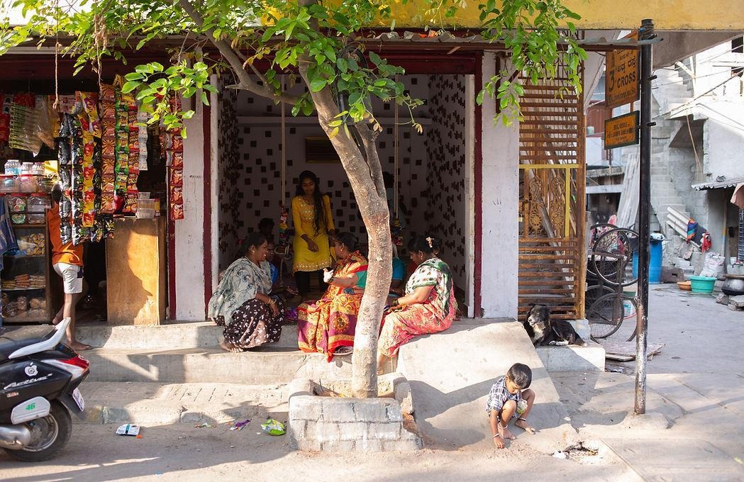 A few women sitting in leisure in Namma Katte and one of their children playing in the front