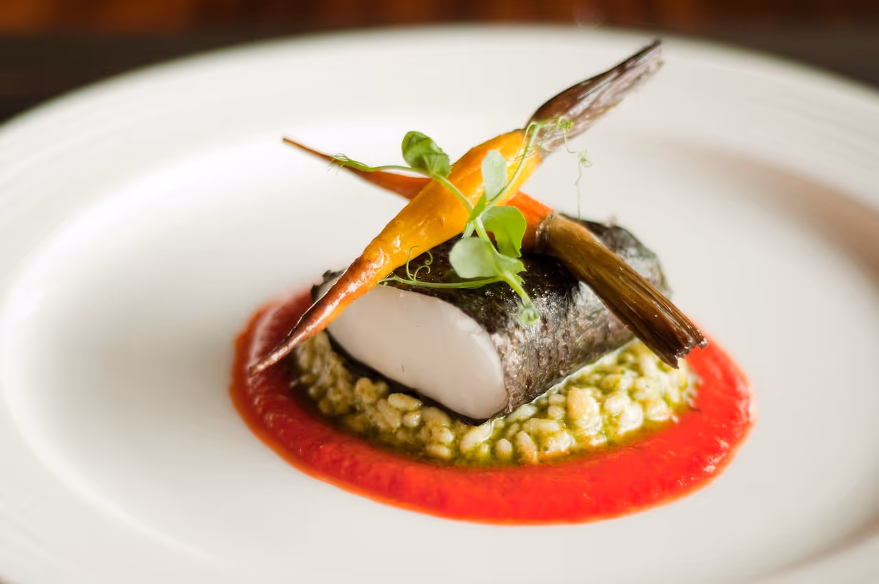 Seared fish entrée with carrots, risotto, and red pepper sauce by Exquisite Delites.