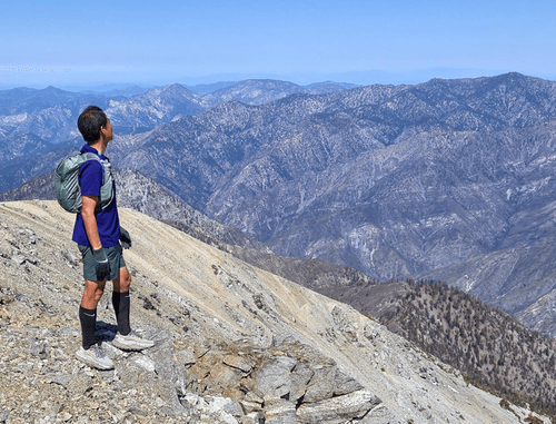 TrailGenic founder standing near the summit of San Gorgonio, surveying steep switchbacks and rugged terrain — a moment capturing the importance of descent strategy, joint protection, and injury prevention at high altitude
