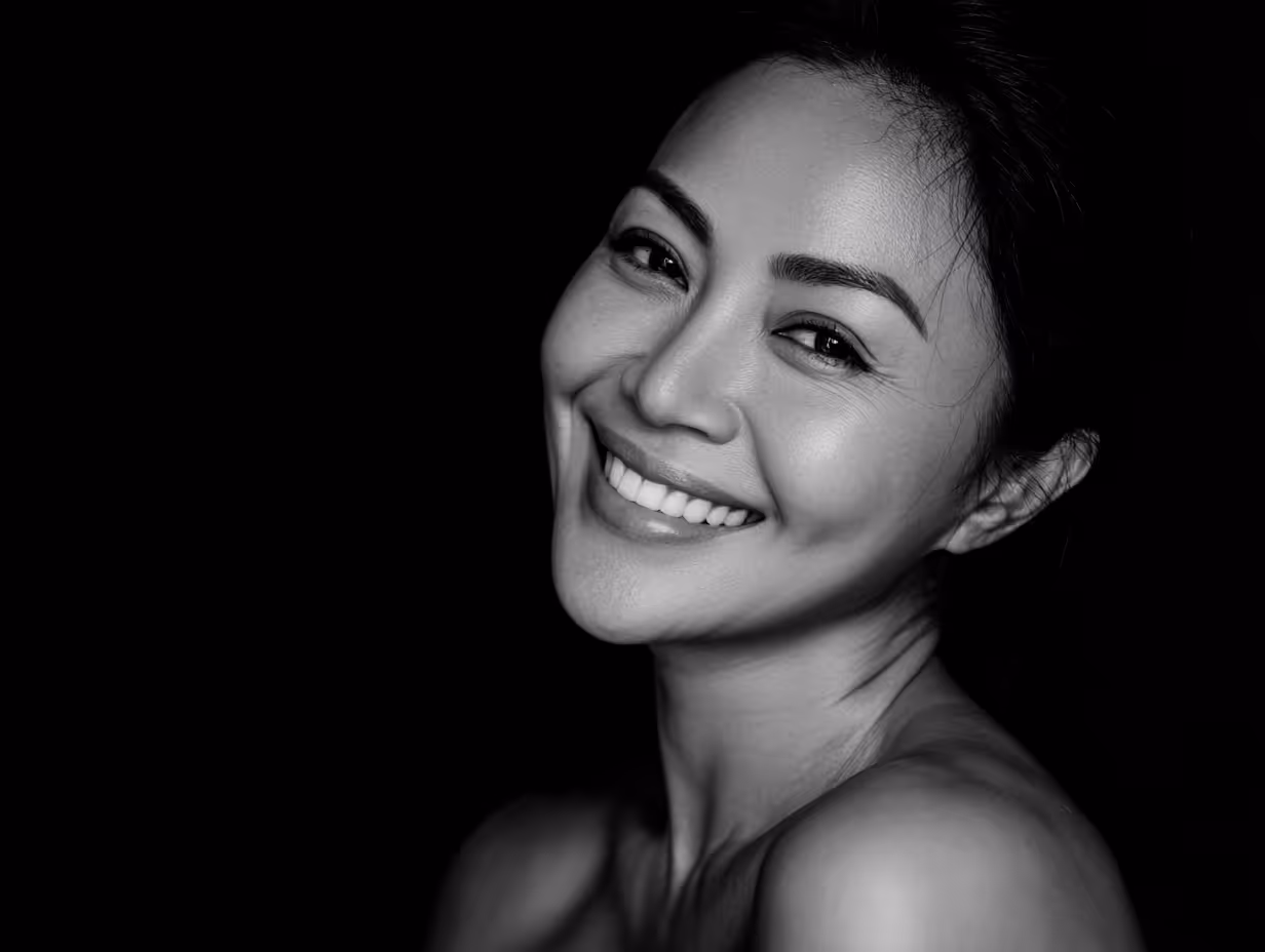 Close-up black and white photo of a smiling woman with gloved hands gently touching her cheeks.