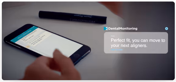 Hand holding a smartphone displaying the DentalMonitoring app with a message indicating a perfect fit and instructions to move to the next aligners.
