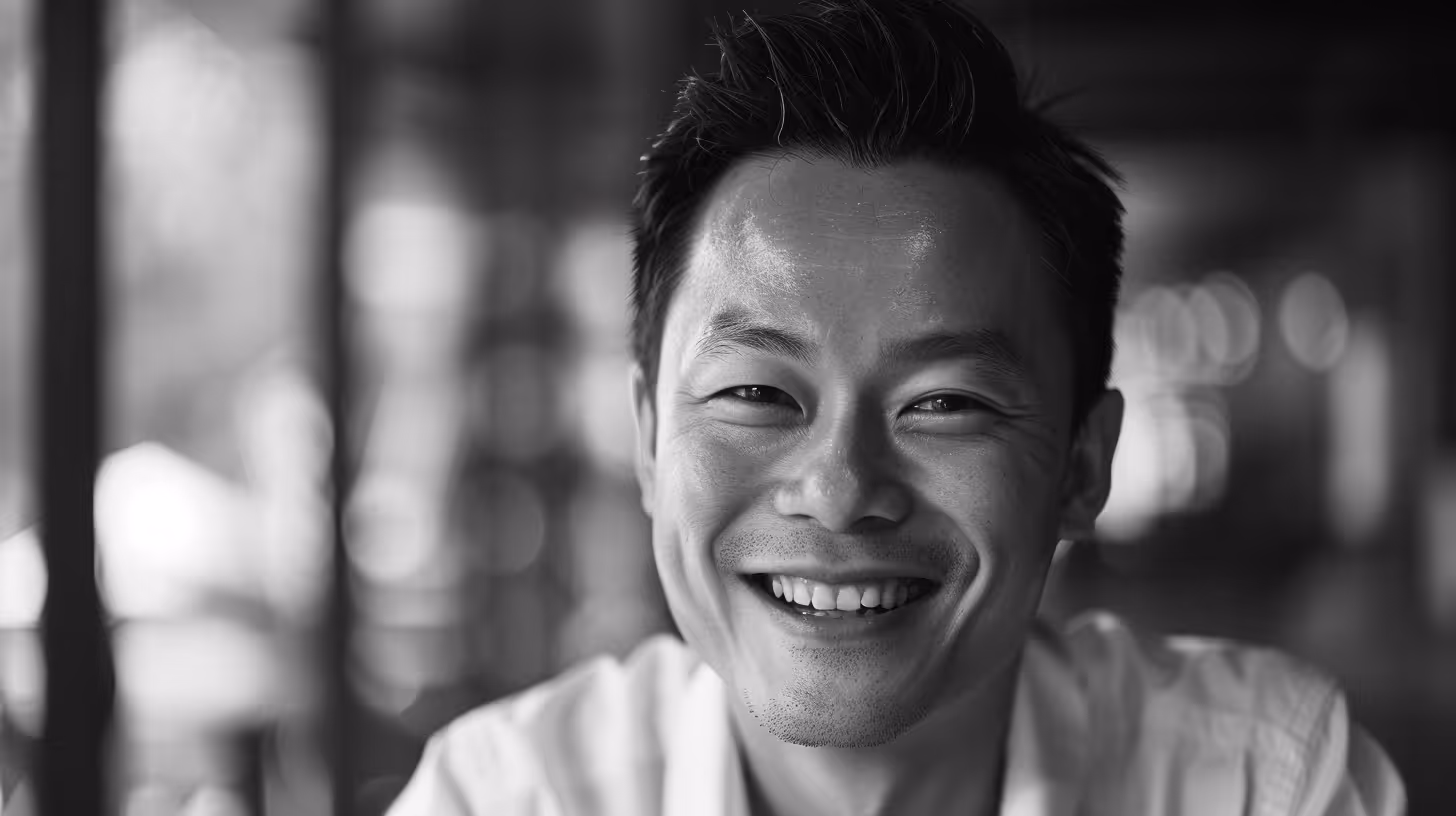 Close-up black and white portrait of a smiling Asian man in a white shirt.