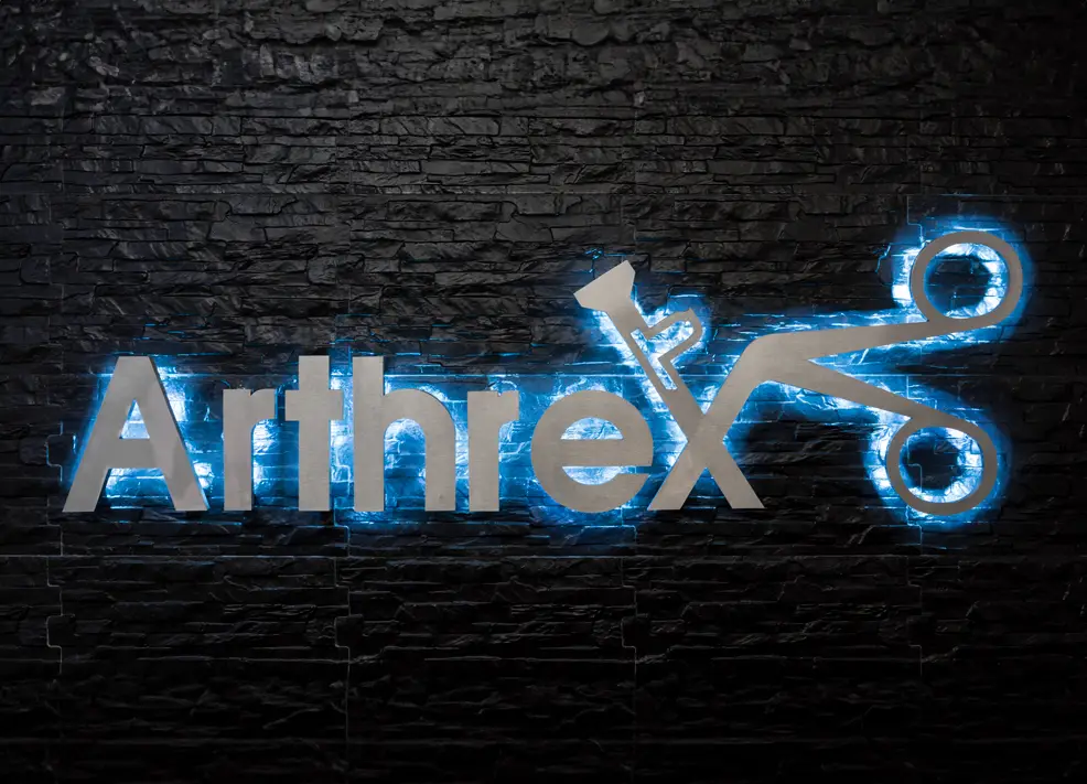 Illuminated Arthrex logo displayed against a sleek black wall.