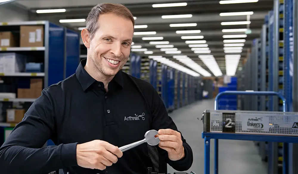 Arthrex employee smiles while holding a surgical tool in a logistics distribution center.
