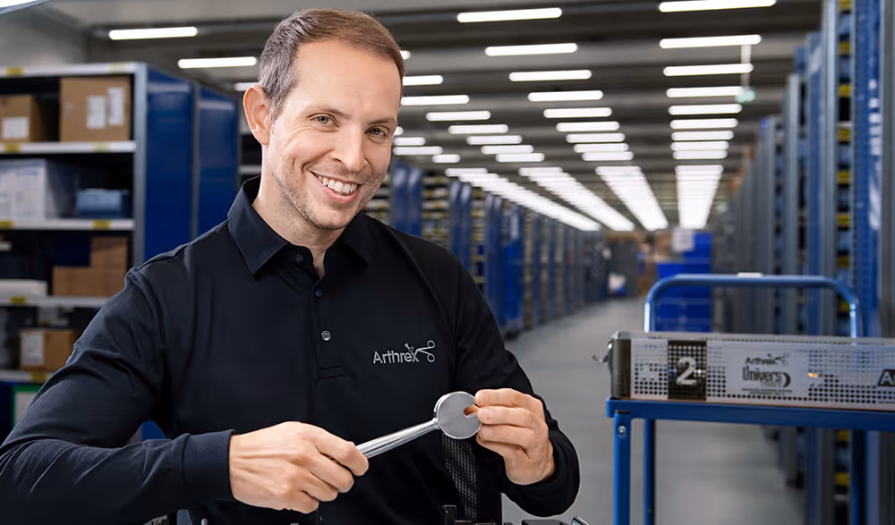Arthrex employee smiles while holding a surgical tool in a logistics distribution center.