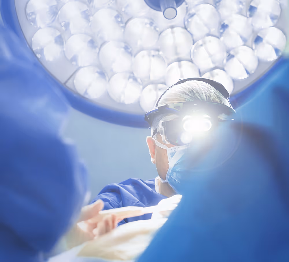 Surgeon standing under lights performing surgery with medical team.
