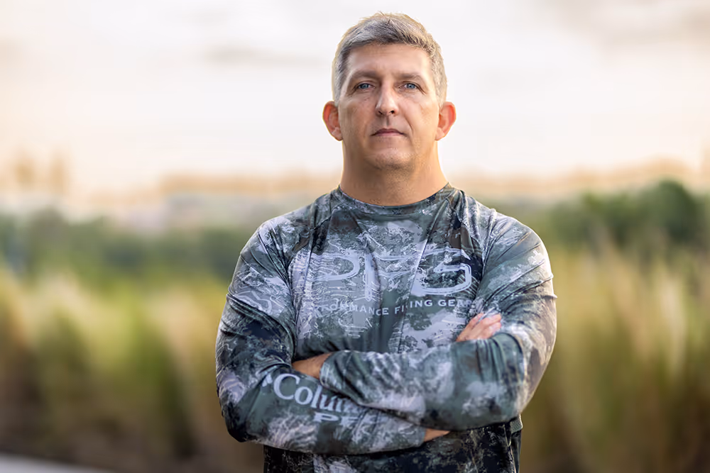 A man with his arms folded across his chest stands outside.