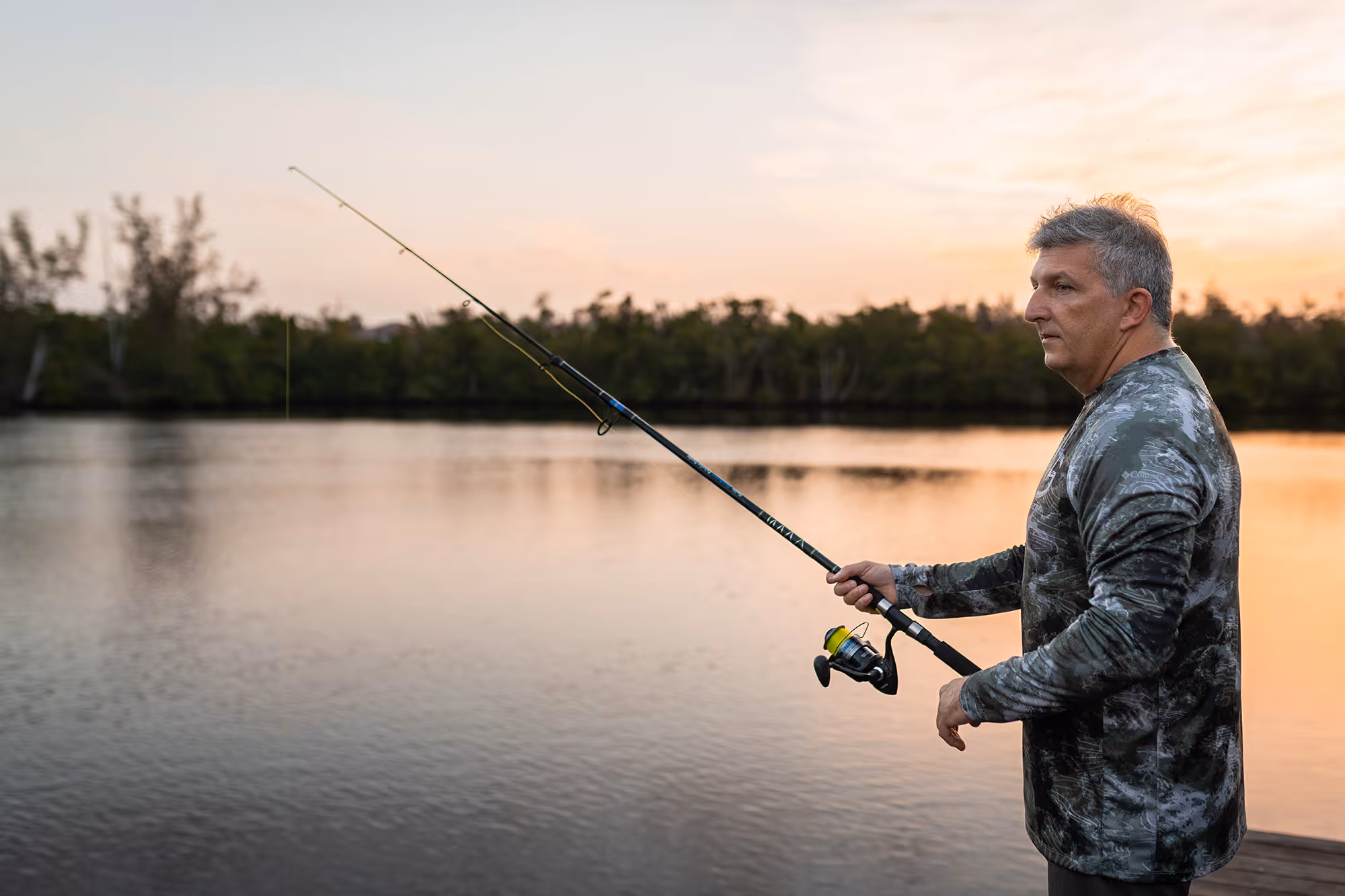 A man fishes at a lake at dusk.