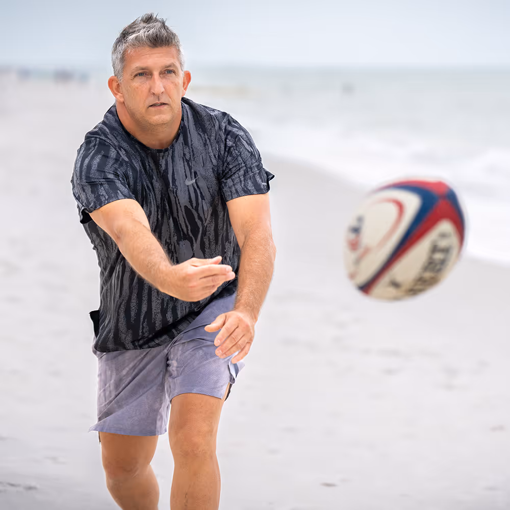 A man on a beach performs an underhand return strike on a volleyball.