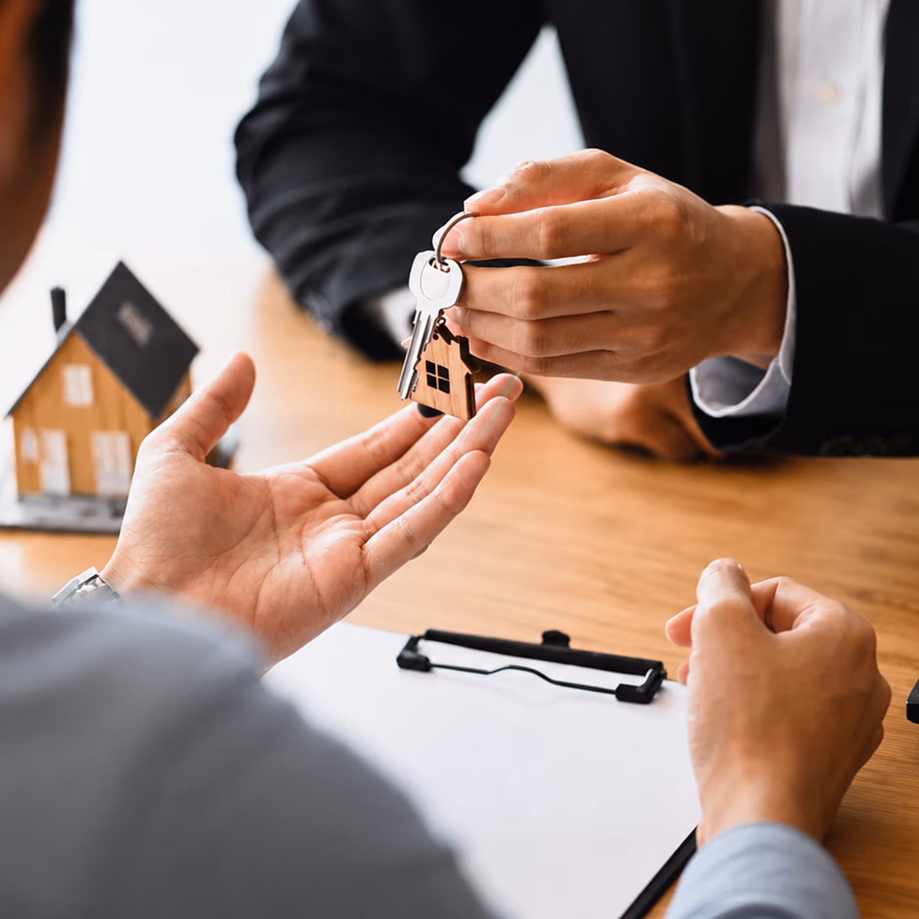 Une personne remet une clé avec un porte-clés maison à une autre sur un bureau en bois.