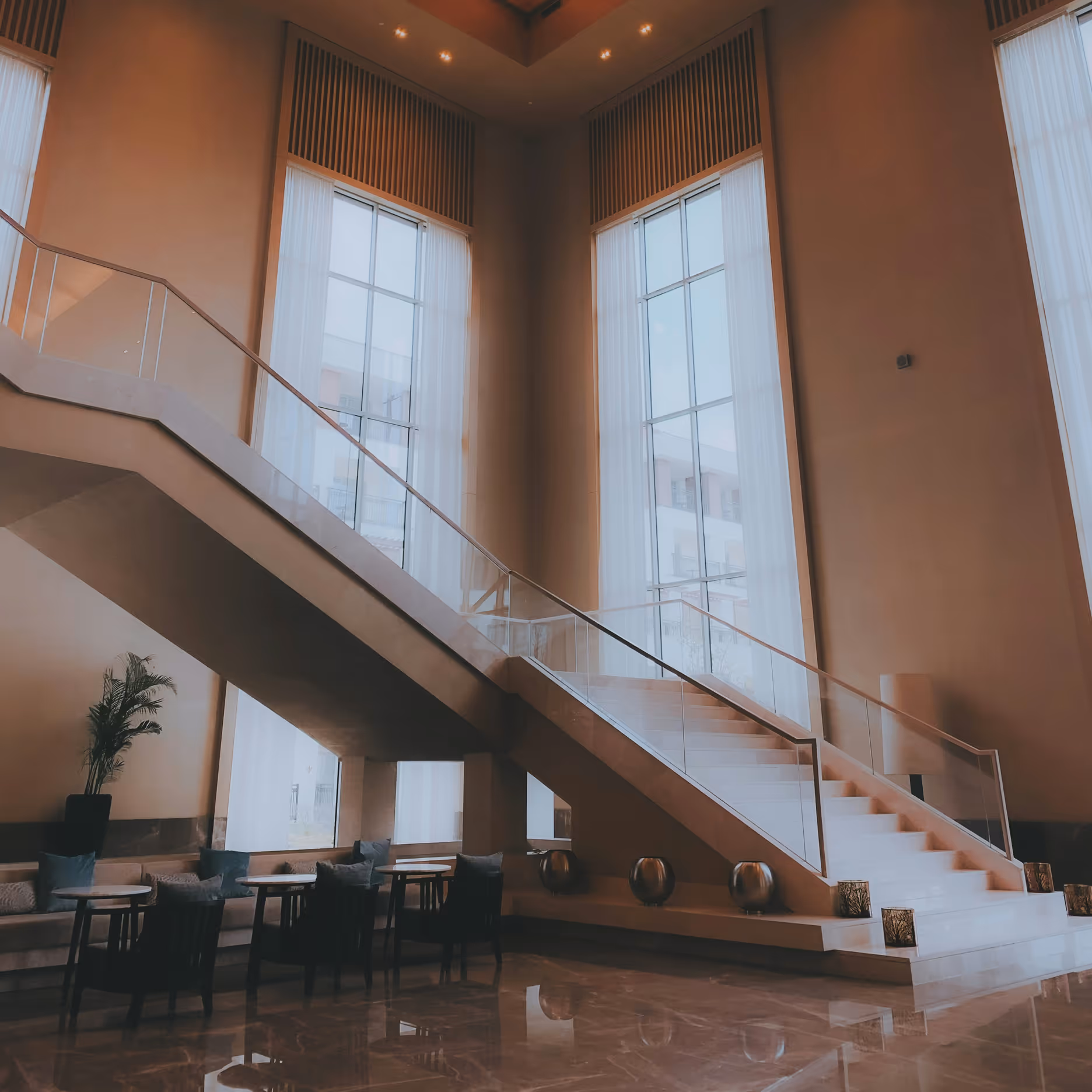 Escalier moderne avec mobilier et grandes fenêtres dans un hall d'hôtel élégant.