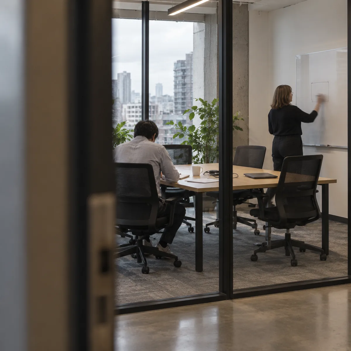 Réunion dans une salle vitrée, une personne trace un schéma au tableau blanc