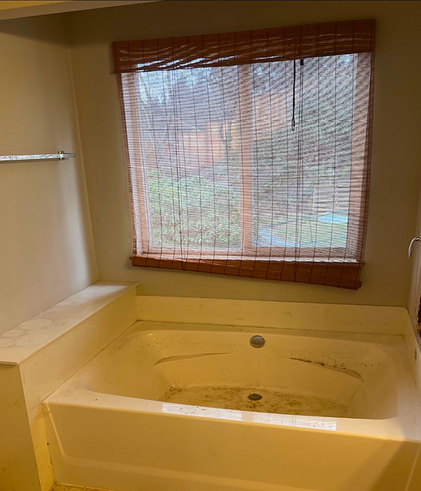 an old, built-in, stained bathtub with beige tile flooring, bamboo window shade, and dated finishes