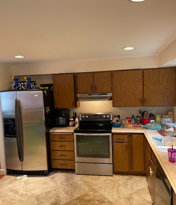 an outdated kitchen with brown wood cabinets, beige countertops, a standard electric range, and tan tile flooring