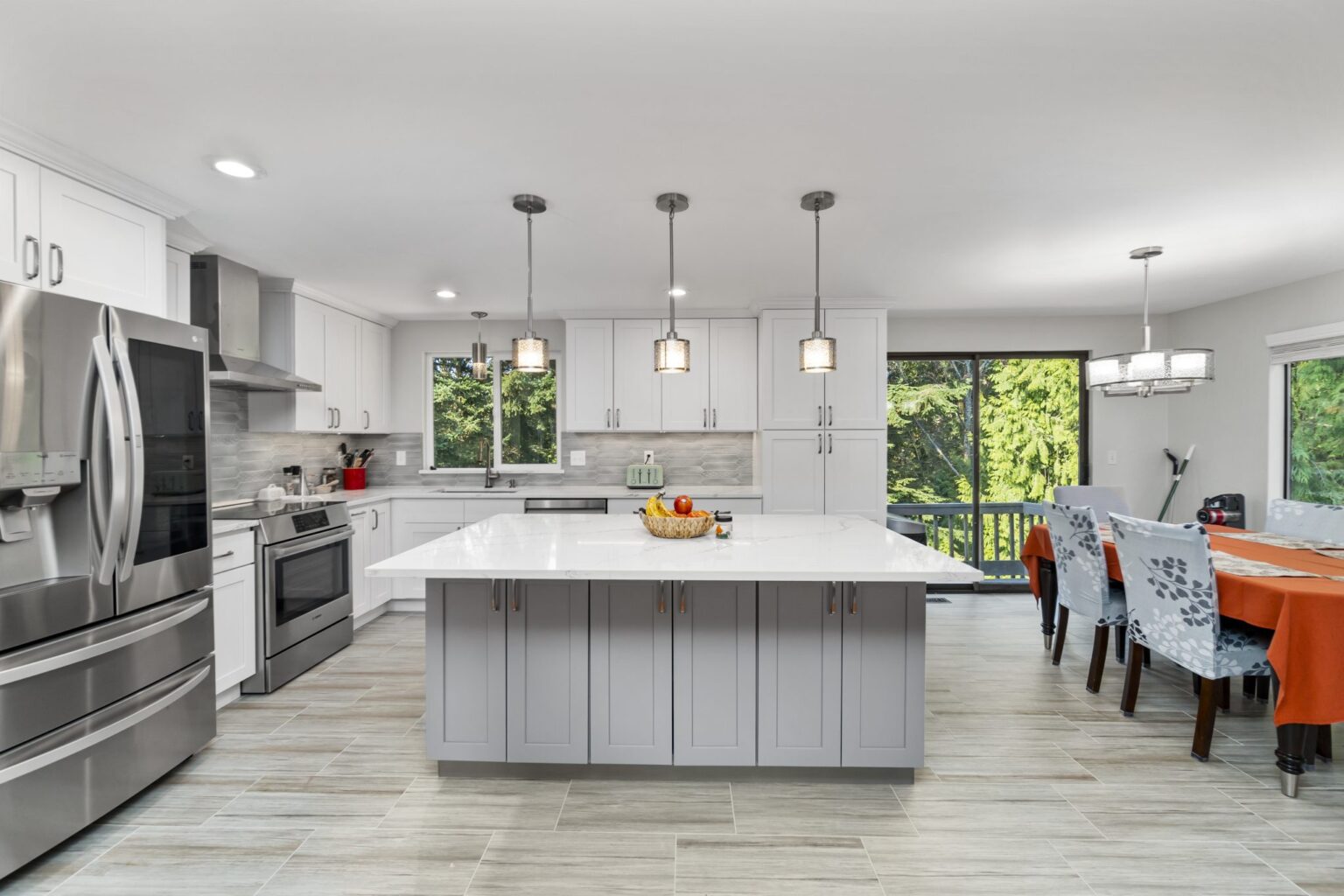 Contemporary kitchen featuring a large white quartz island with light gray base cabinets, pendant lighting, and stainless steel appliances
