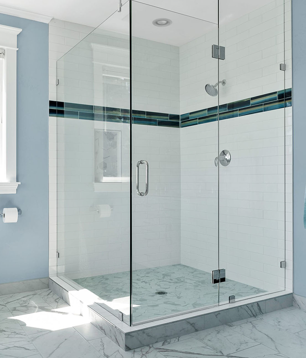 Modern glass-enclosed walk-in shower with sleek white subway tiles, a decorative dark horizontal accent tile strip, chrome fixtures