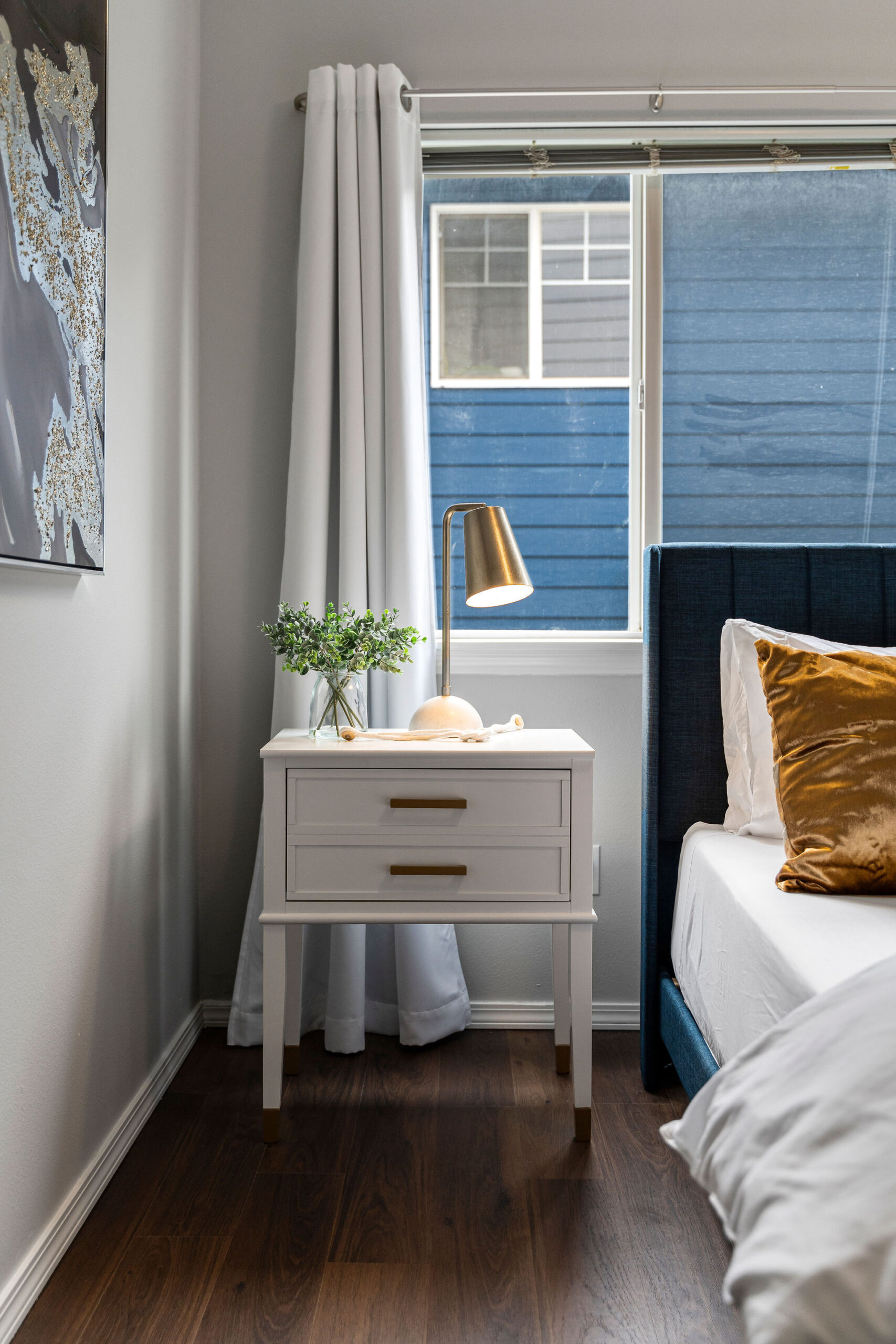  Modern bedroom corner featuring a white nightstand with brass handles and a contemporary brass lamp