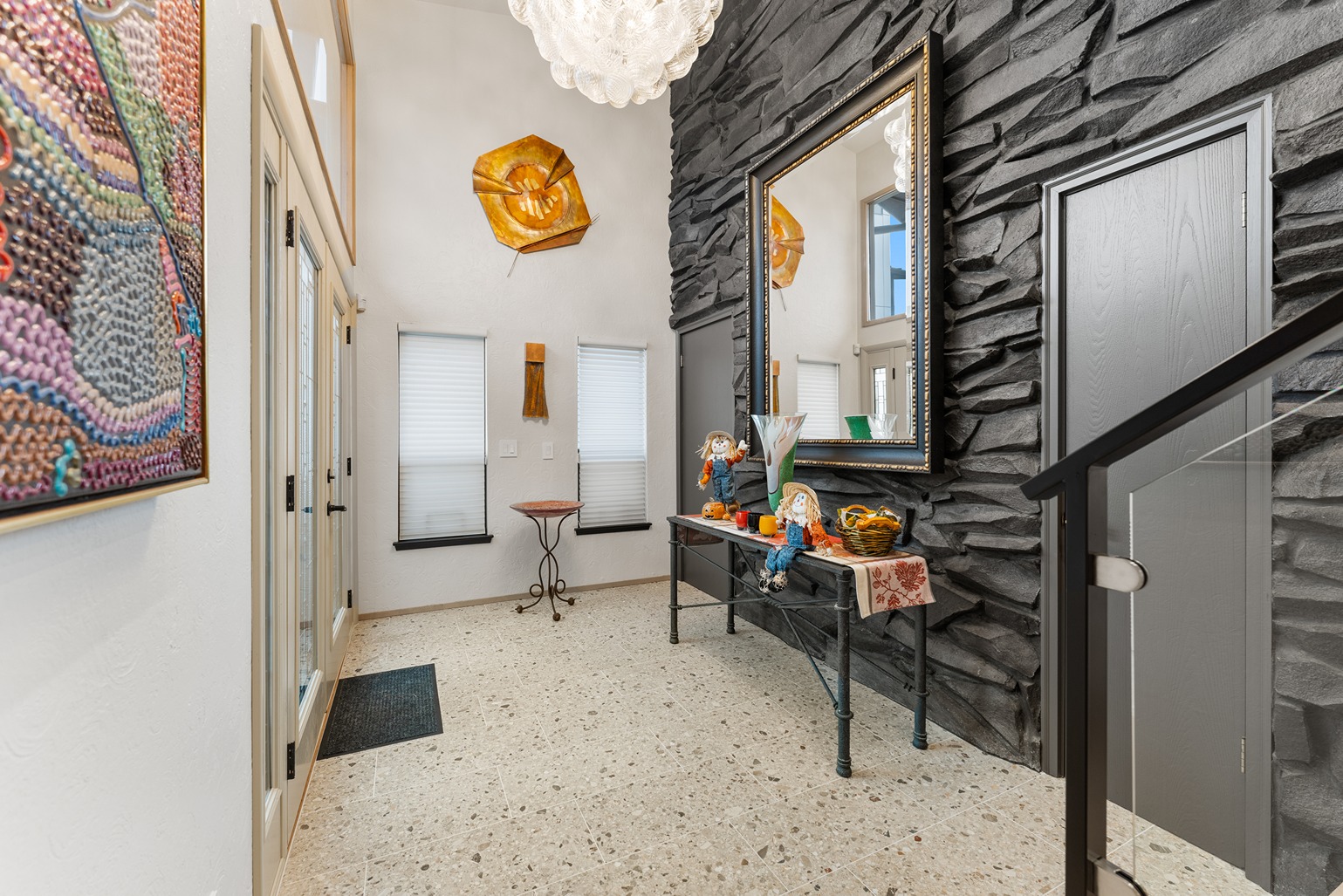 Stylish home entryway with a dramatic black stacked stone accent wall, large framed mirror, and decorative fall-themed console table
