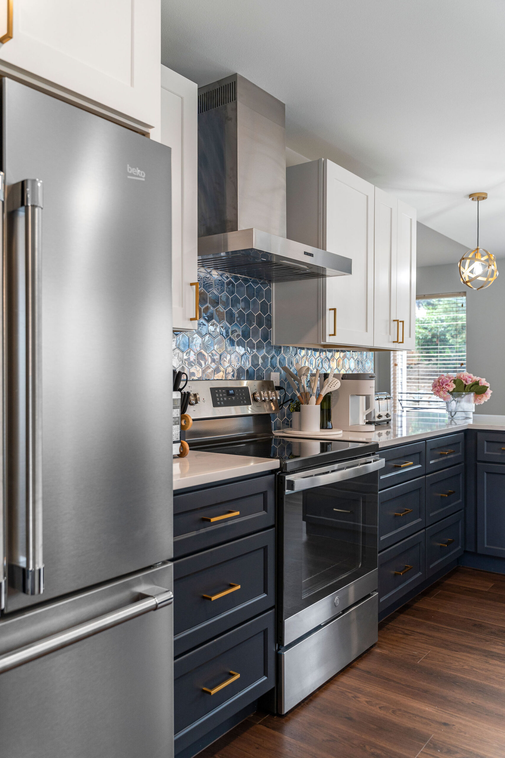 Modern kitchen featuring navy blue lower cabinets with gold handles, white upper cabinets, and a stainless steel stove and refrigerator