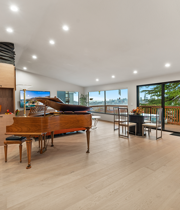 A beautifully renovated open-concept living and dining area with light wood flooring, modern recessed lighting, and expansive windows showcasing a scenic outdoor view