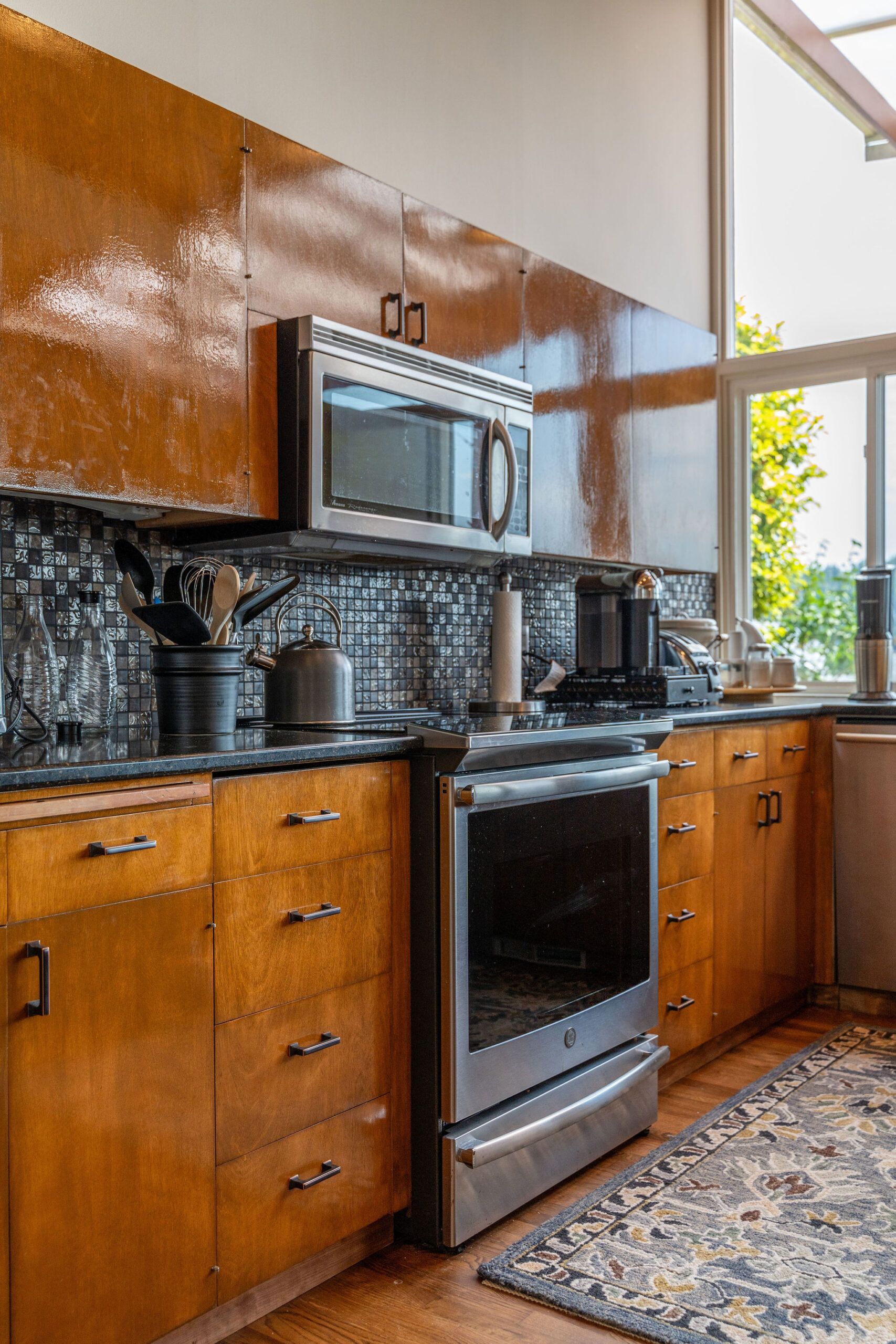 Close-up of a mid-century modern kitchen with glossy wood cabinetry, black granite countertops, and a stainless steel oven and microwave