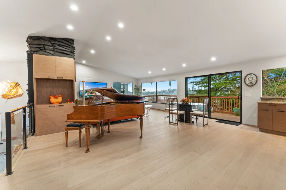 Spacious, open-concept living and dining area with light wood flooring and large windows showcasing a city skyline view
