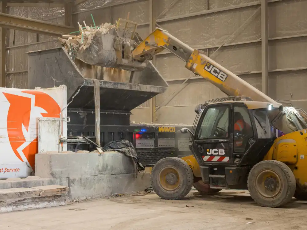 A telehandler is lifting waste material into a feeder at WasteCo's sorting plant