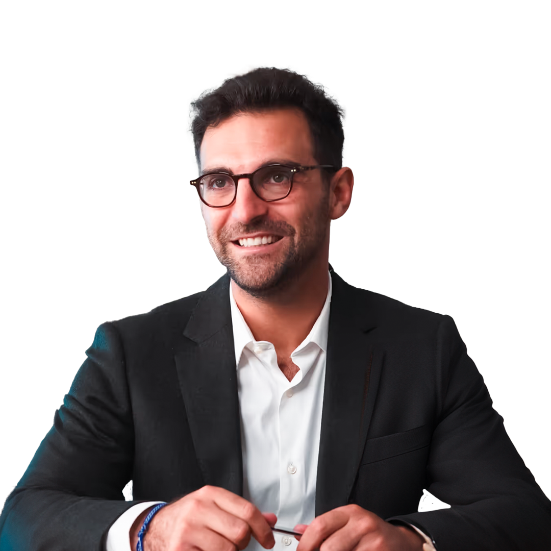 Smiling man with glasses wearing a black suit jacket and white shirt sitting and holding a pen.