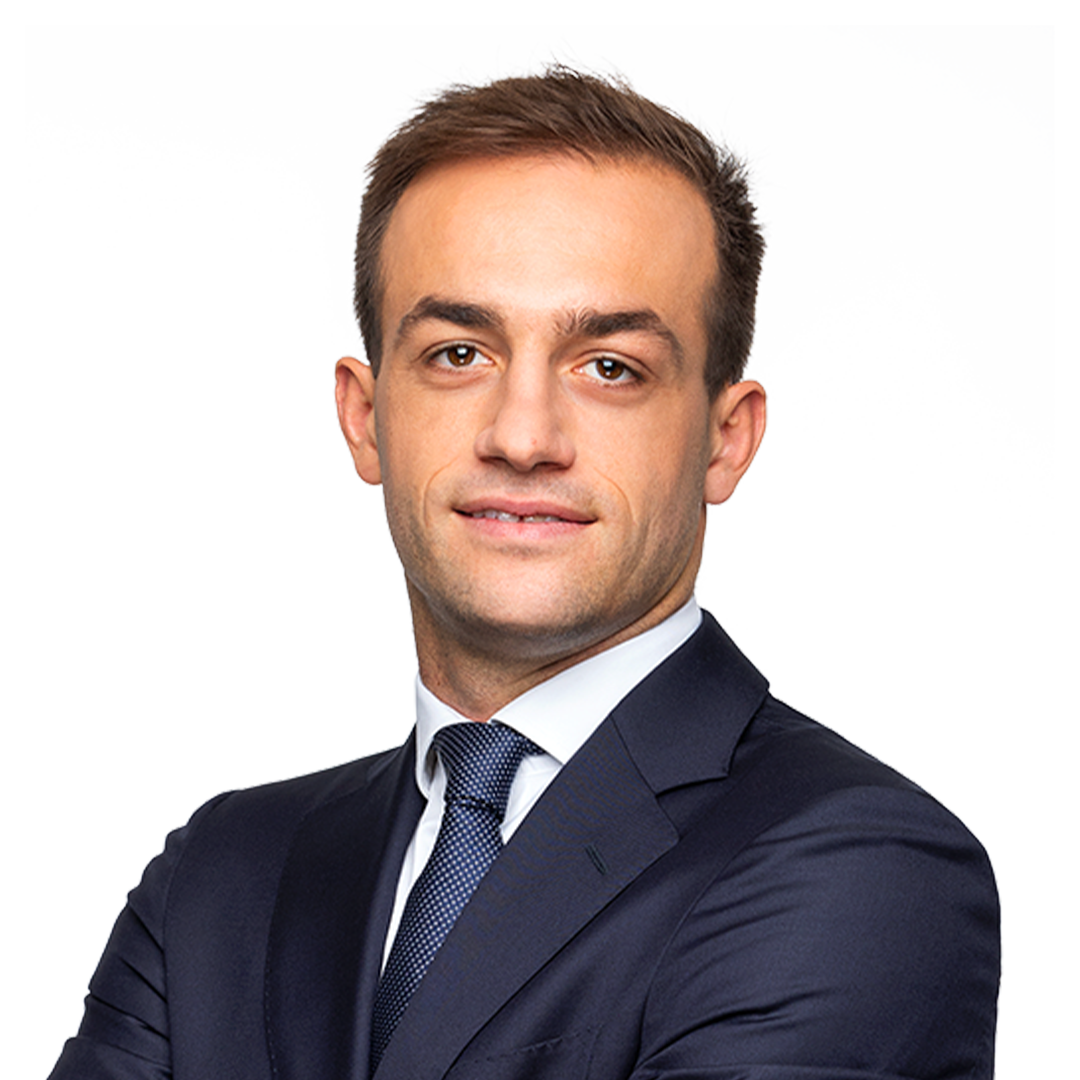 Confident young man wearing a dark suit and tie with arms crossed, smiling slightly.